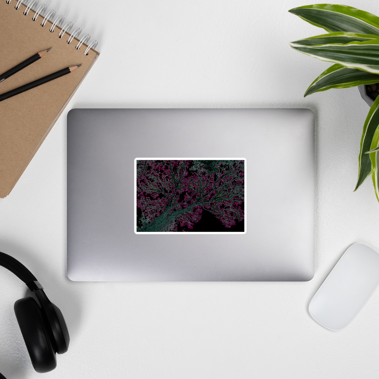 Lifestyle photo of a rectangular vinyl sticker with an image of a neon pink and turquoise tree design with lightning like features, placed on the outside of a laptop.