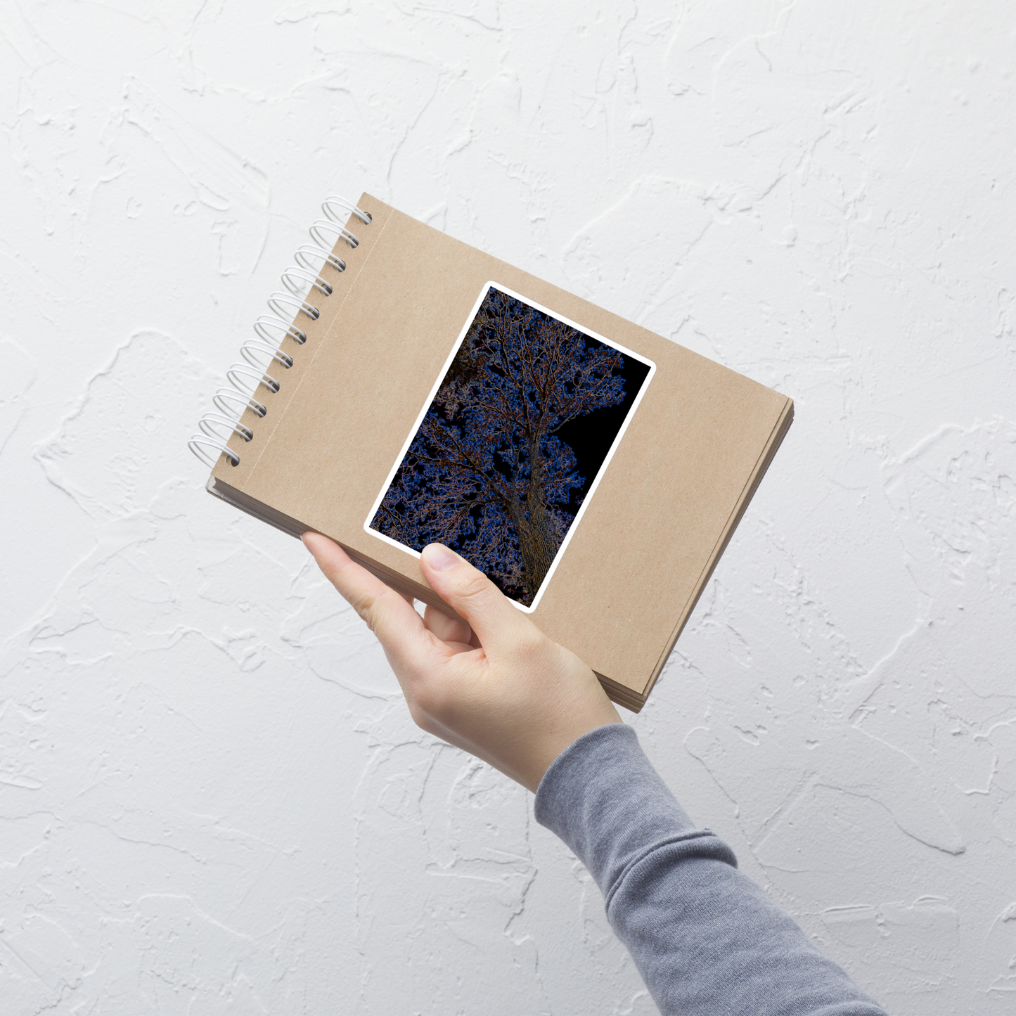 Lifestyle photo of a rectangular vinyl sticker with an image of a neon blue and yellow tree design with lightning like features, placed on a small notepad.
