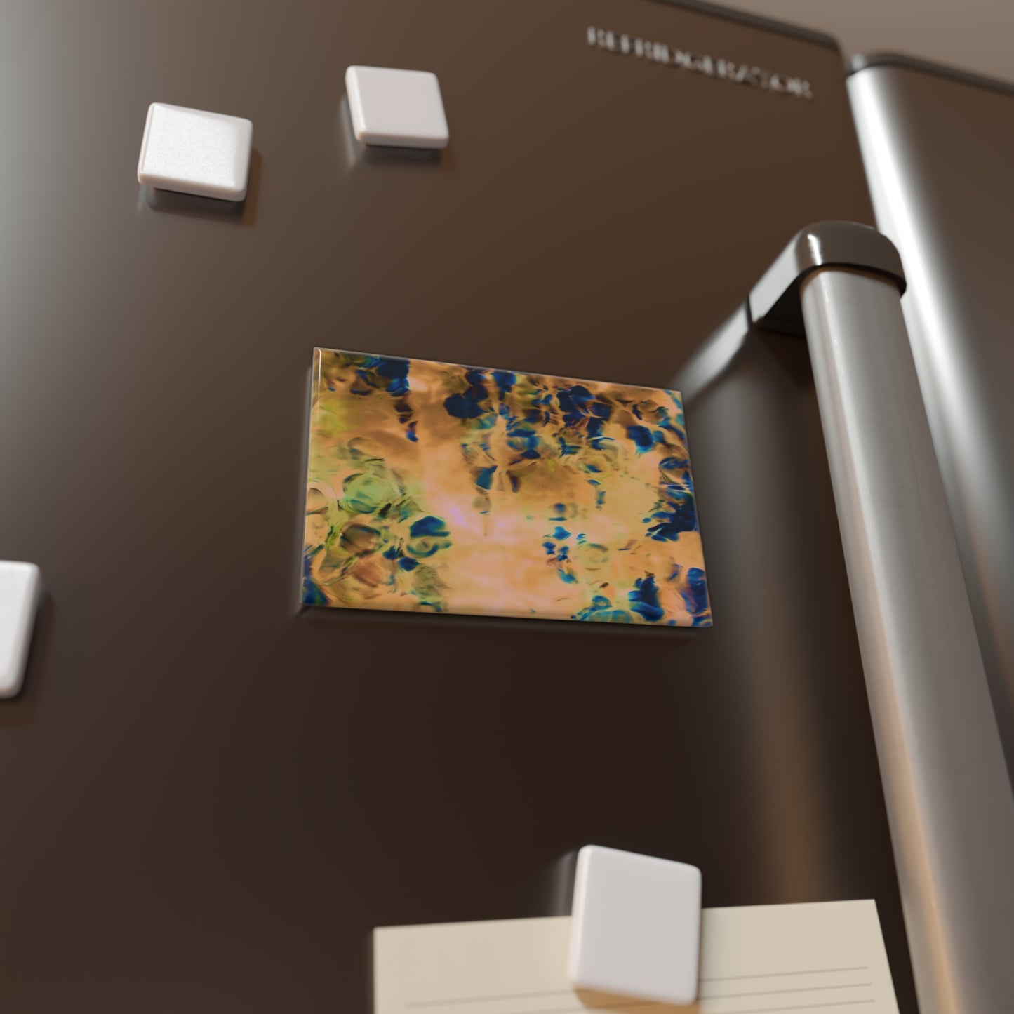 Lifestyle photo of a rectangular button magnet with an image of a vivid orange and blue water reflection design, placed on a fridge.