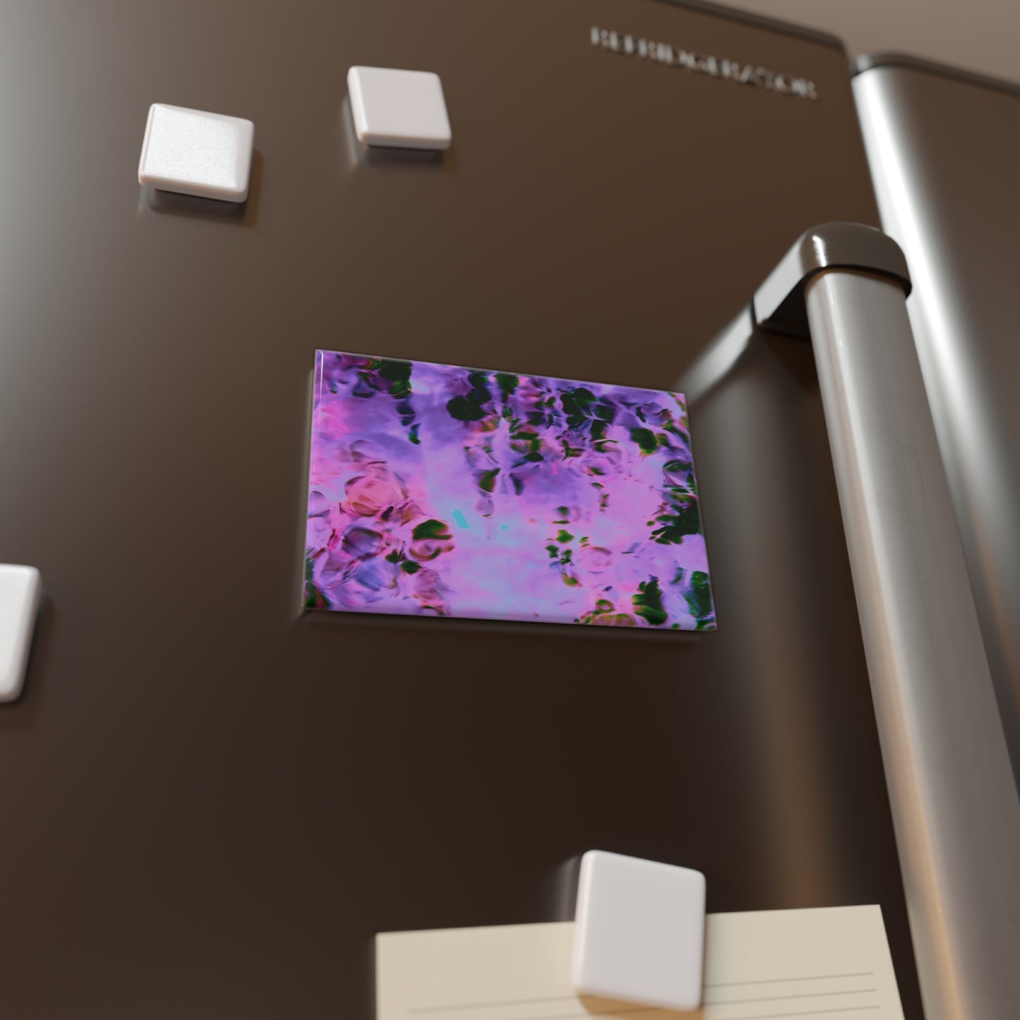 Lifestyle photo of a rectangular button magnet with an image of a vivid pink and purple water reflection design, placed on a fridge.