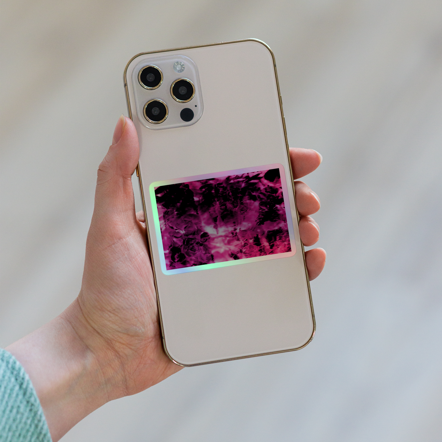 Lifestyle photo of a rectangular holographic sticker with an image of a vivid pink and black water reflection design, placed on the back of a phone.