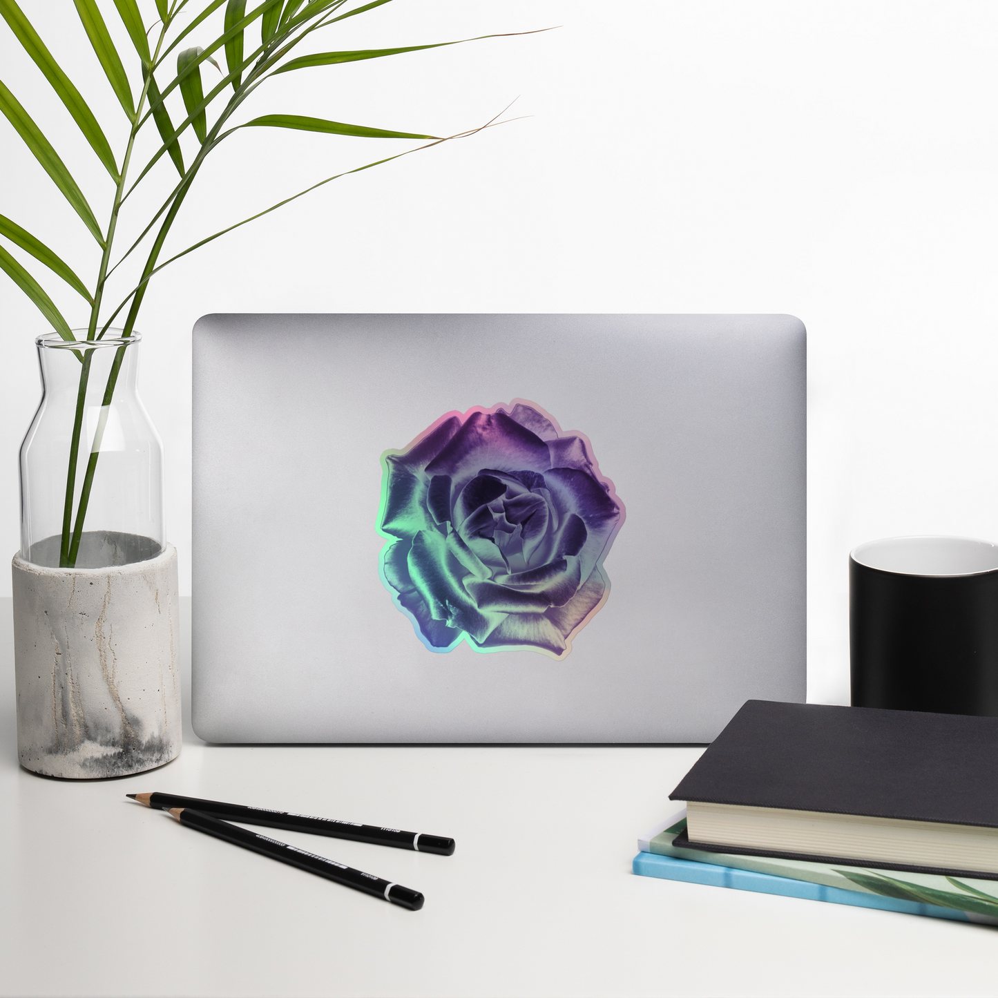 Lifestyle photo of a kiss-cut holographic sticker with an image of a reflective purple rose design, placed on a laptop with desk supplies nearby.