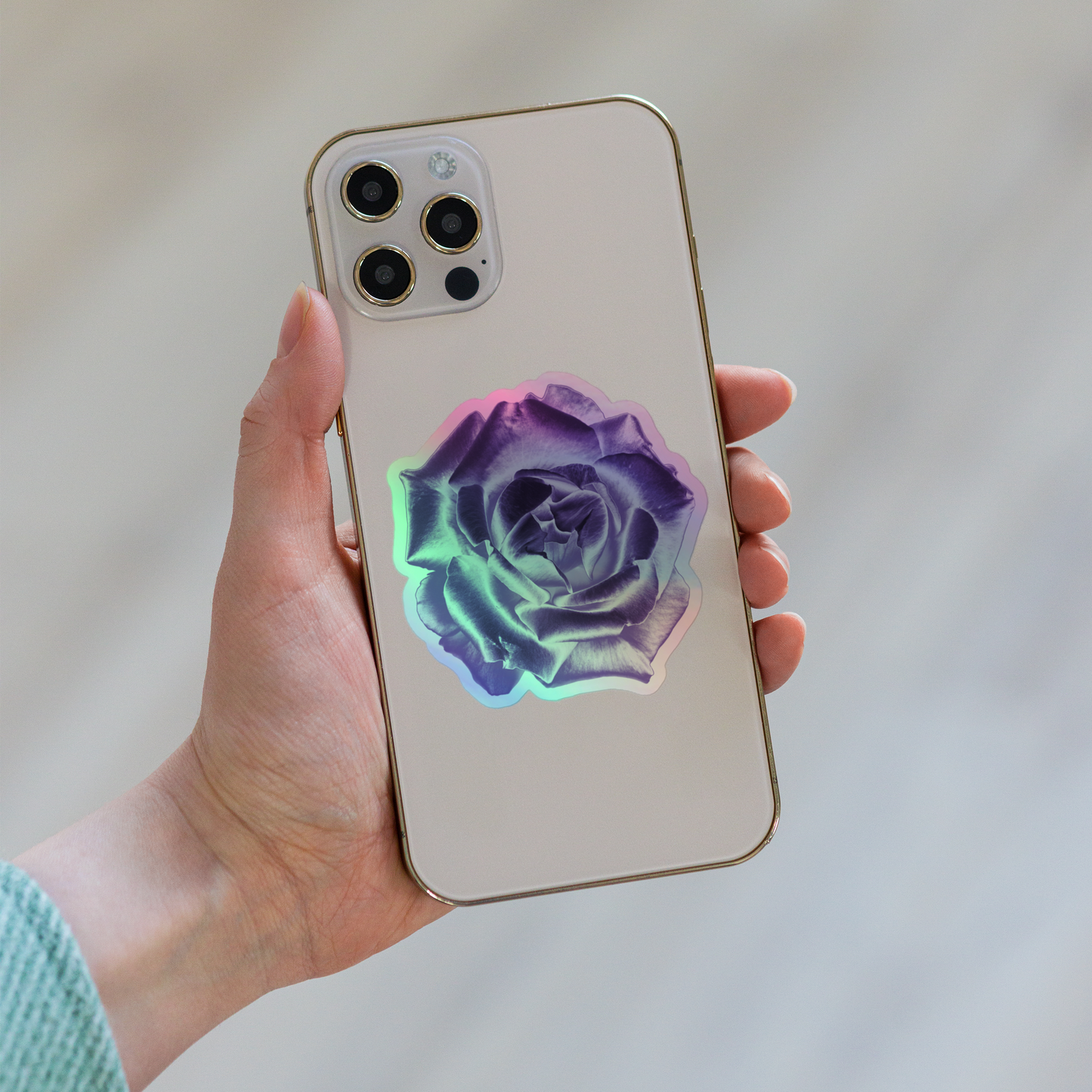 Lifestyle photo of a kiss-cut holographic sticker with an image of a reflective purple rose design, placed on the back of a phone.