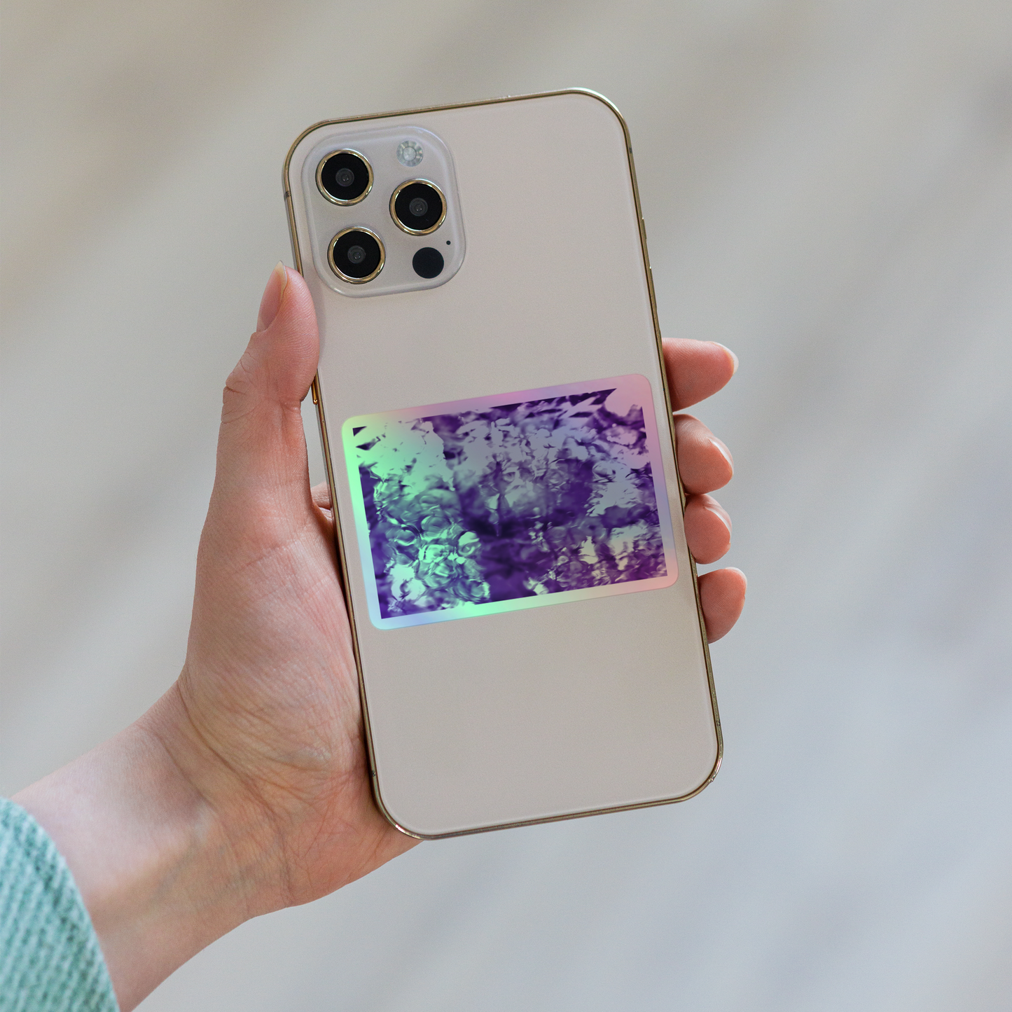 Lifestyle photo of a rectangular holographic sticker with an image of a vivid purple water reflection design, placed on the back of a phone.