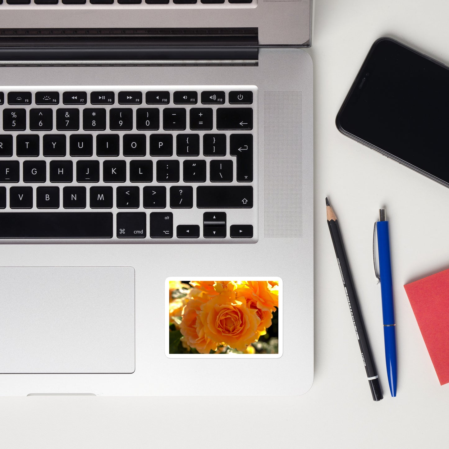 Lifestyle photo of a rectangular vinyl sticker with an image of orange rose blooms, placed on a laptop to the right of the mouse pad.