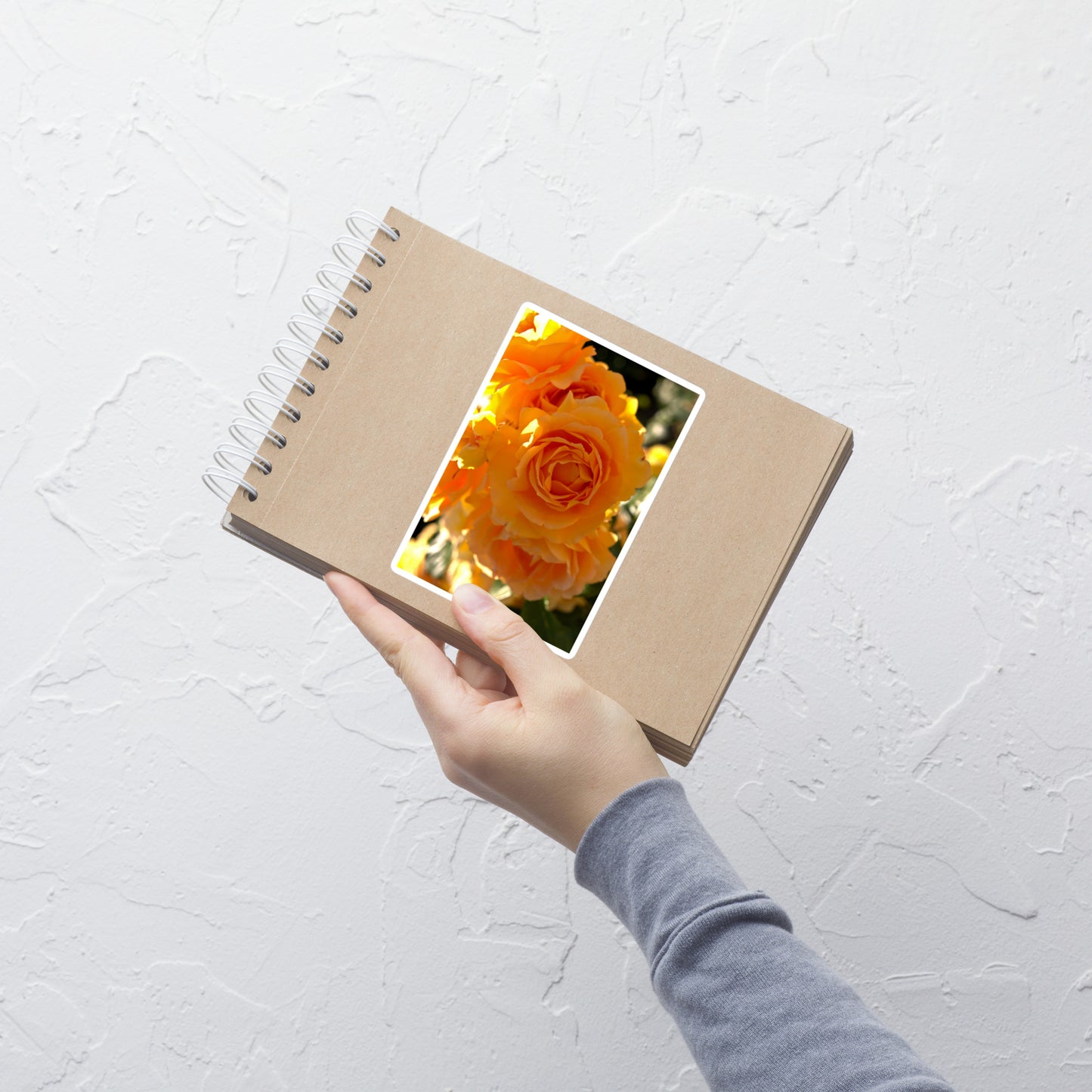 Lifestyle photo of a rectangular vinyl sticker with an image of orange rose blooms, placed on a small notepad.