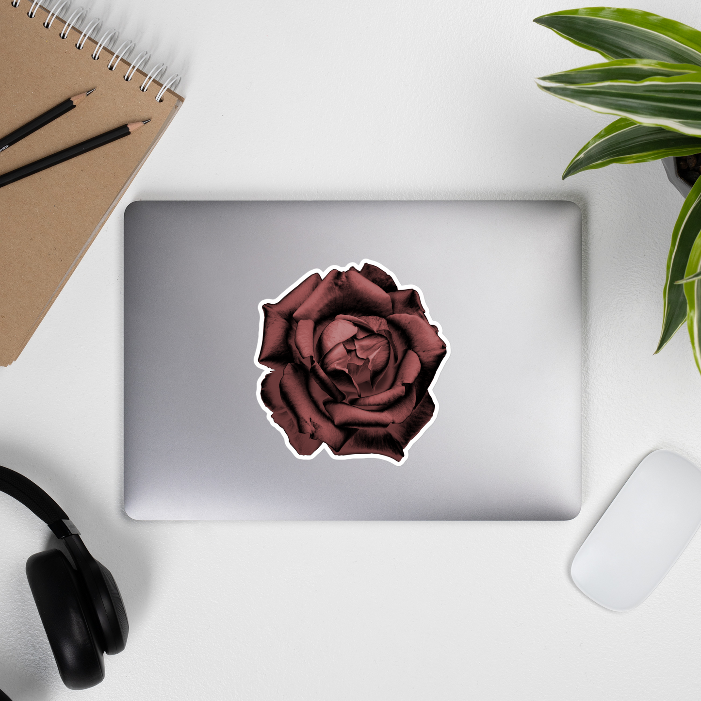 Lifestyle photo of a kiss-cut vinyl sticker with an image of a red charcoal drawing style rose, placed on the outside of a laptop.