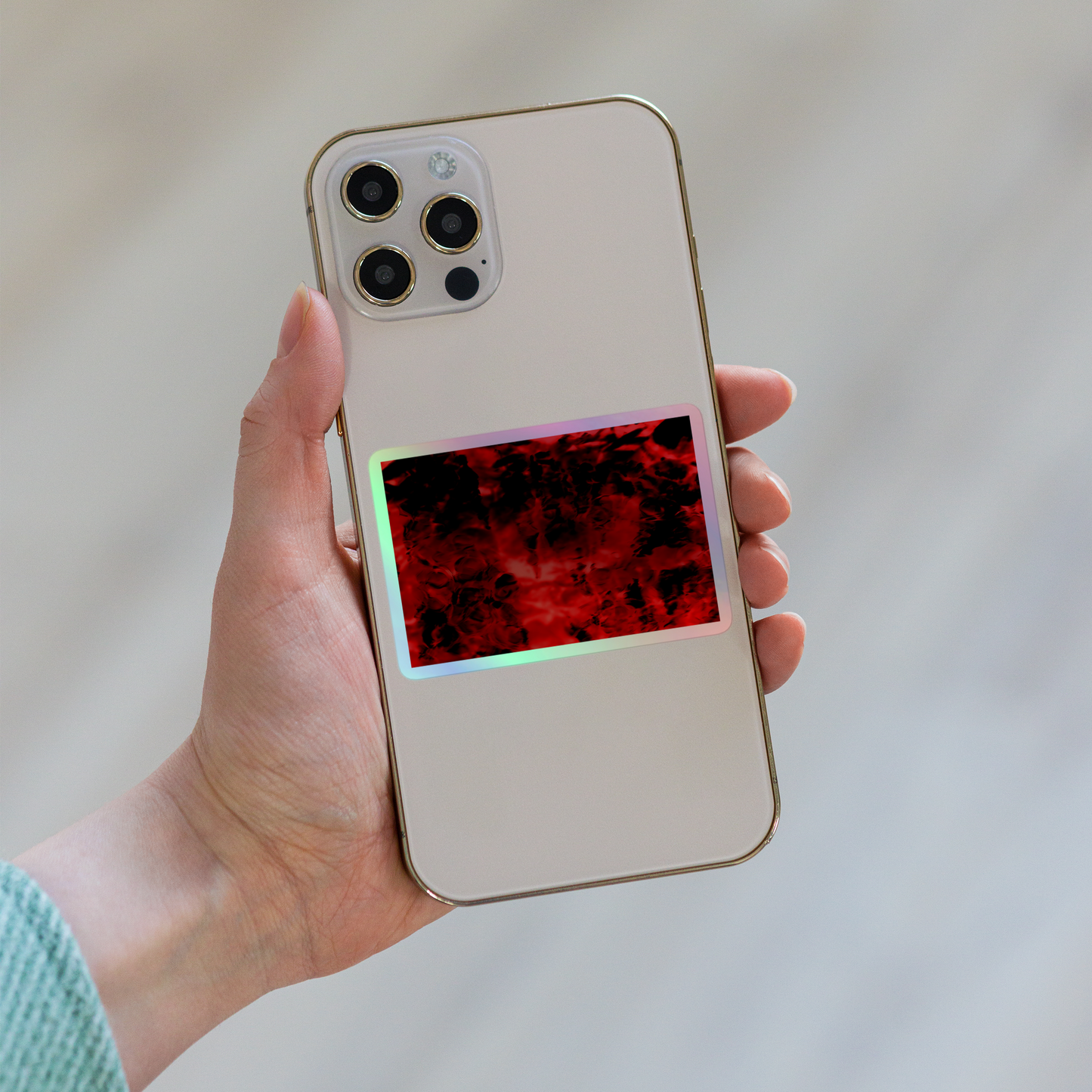 Lifestyle photo of a rectangular holographic sticker with an image of a vivid red and black water reflection design, placed on the back of a phone.