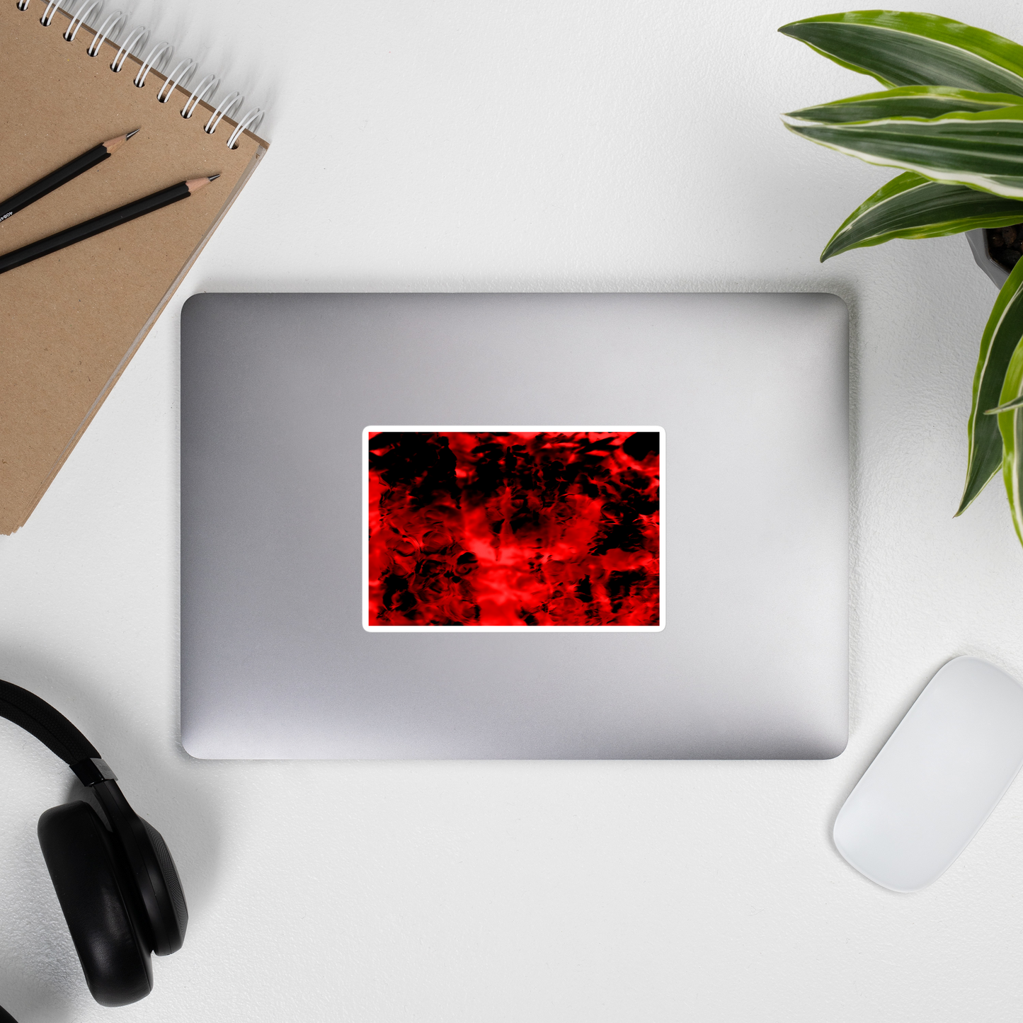 Lifestyle photo of a rectangular vinyl sticker with an image of a vivid red and black water reflection design, placed on the outside of a laptop.