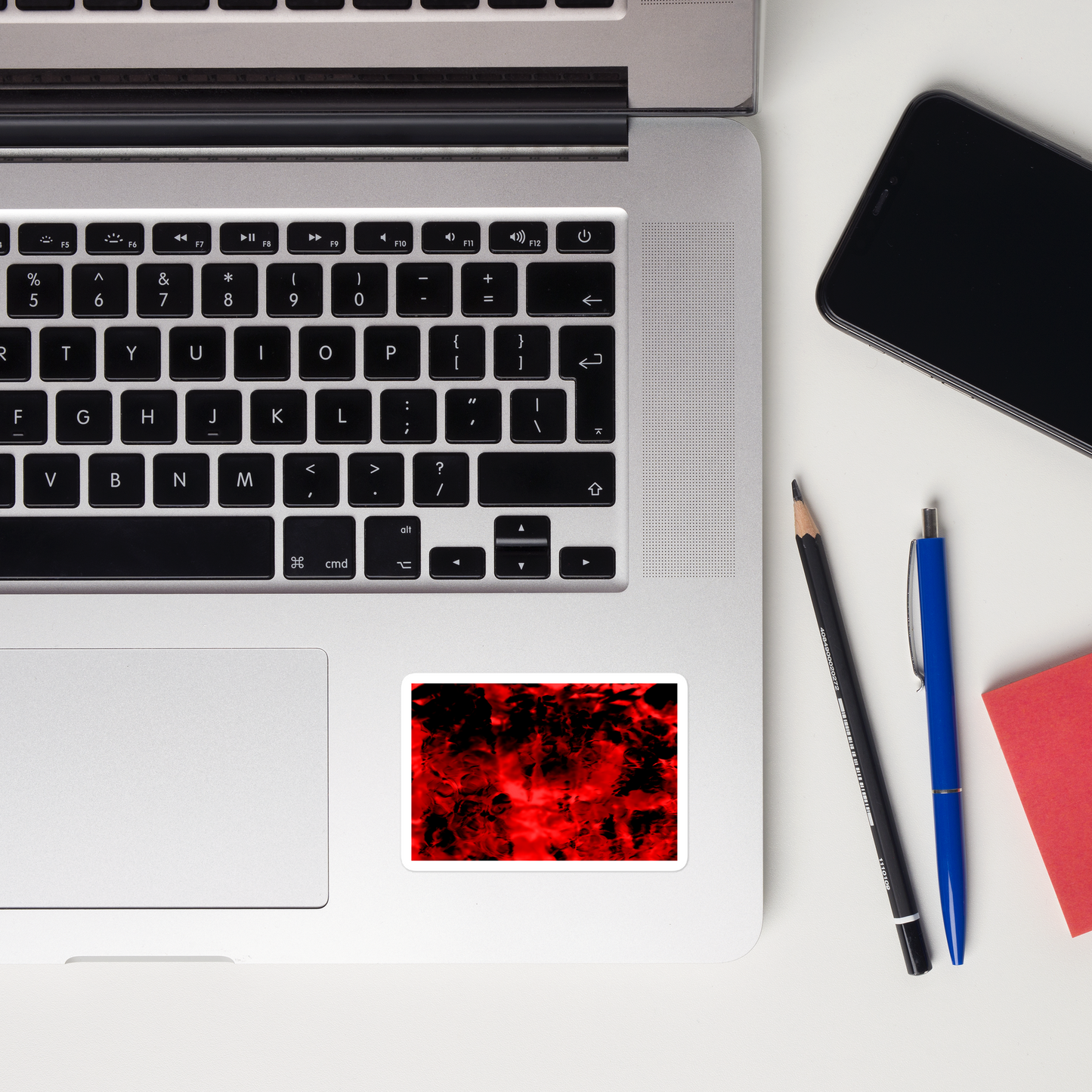 Lifestyle photo of a rectangular vinyl sticker with an image of a vivid red and black water reflection design, placed on a laptop to the right of the mouse pad.