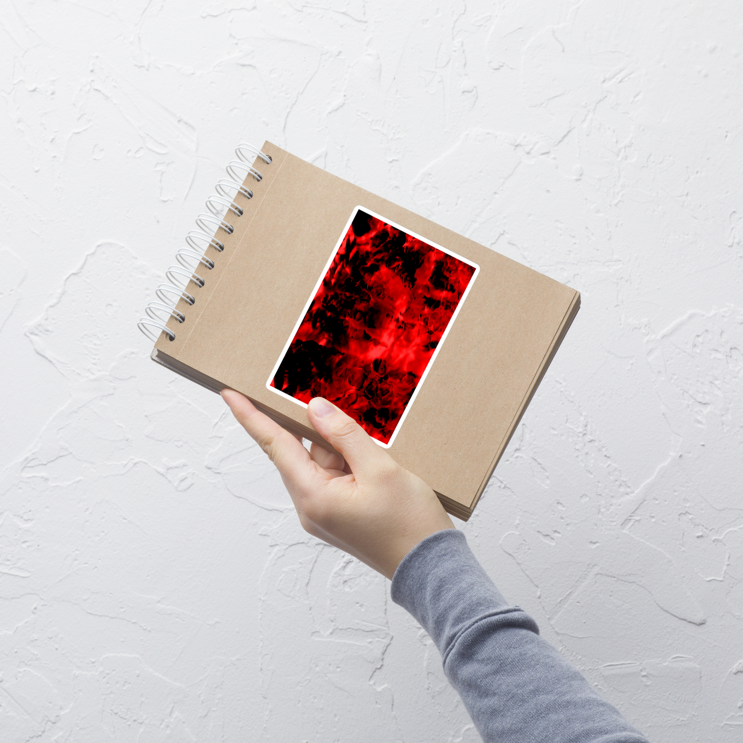Lifestyle photo of a rectangular vinyl sticker with an image of a vivid red and black water reflection design, placed on a small notepad.