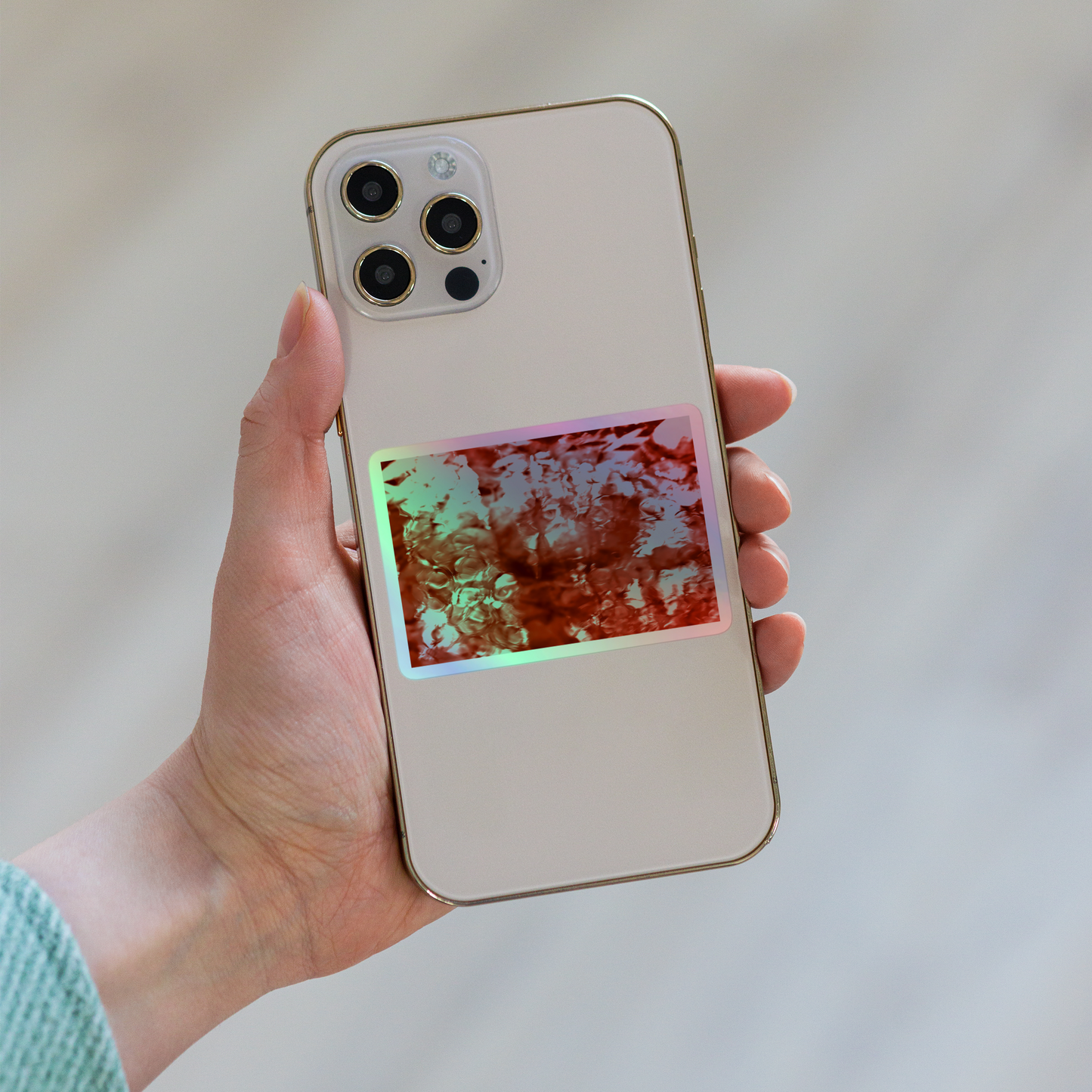 Lifestyle photo of a rectangular holographic sticker with an image of a vivid red water reflection design, placed on the back of a phone.