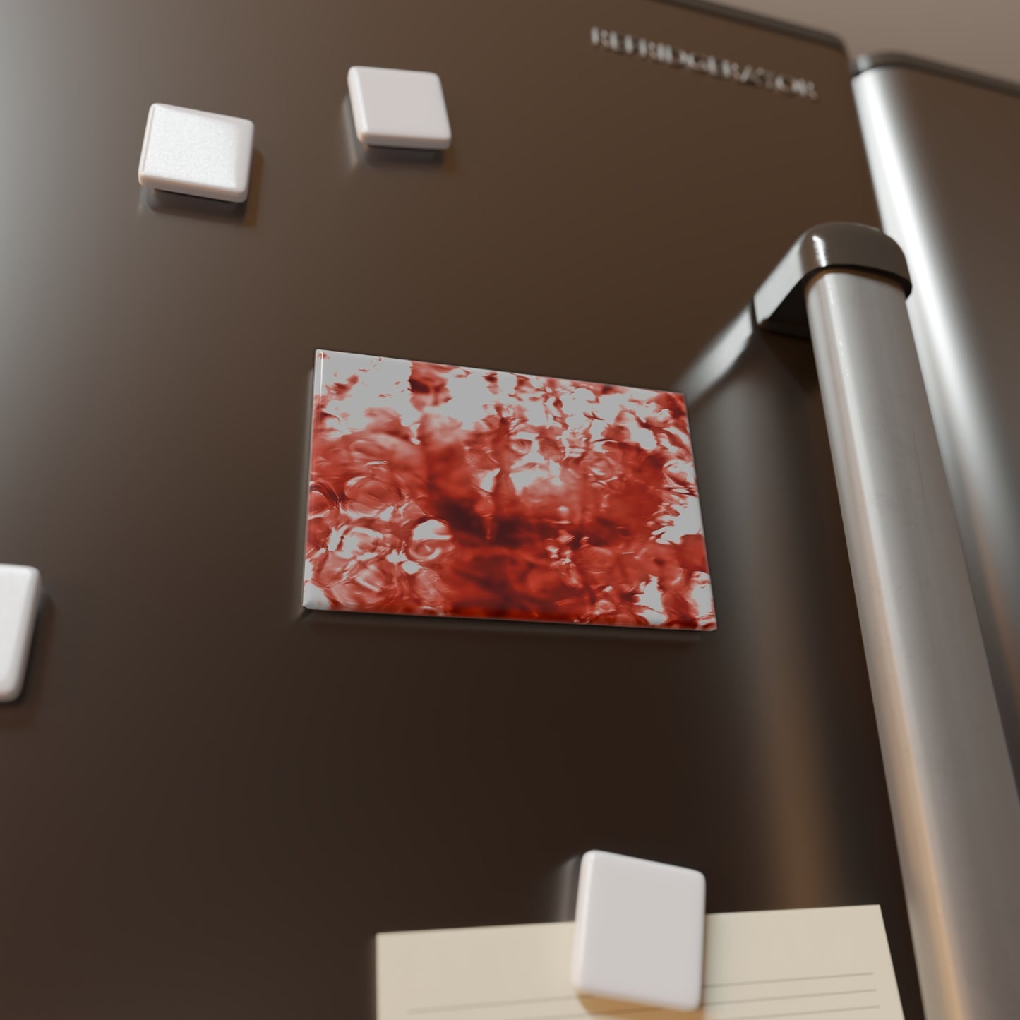 Lifestyle photo of a rectangular button magnet with an image of a vivid red water reflection design, placed on a fridge.