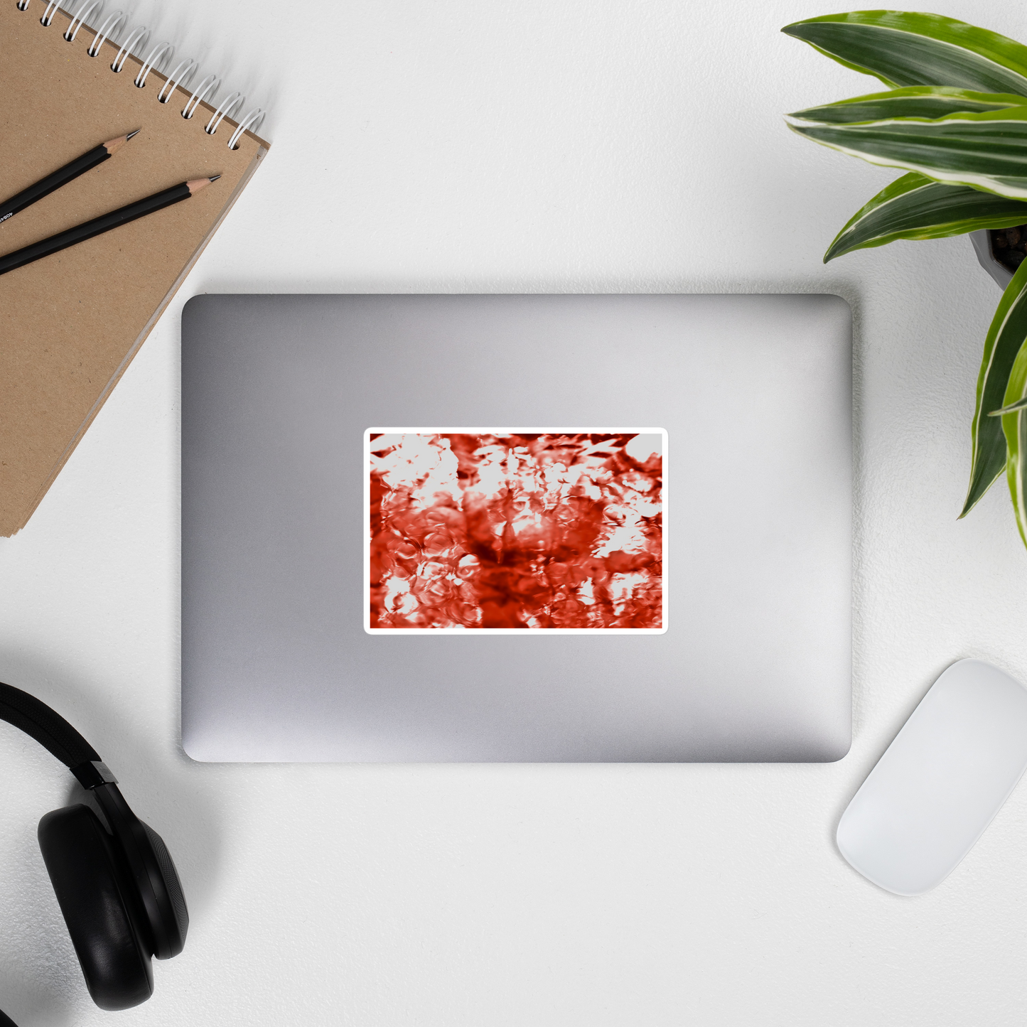 Lifestyle photo of a rectangular vinyl sticker with an image of a vivid red water reflection design, placed on the outside of a laptop.