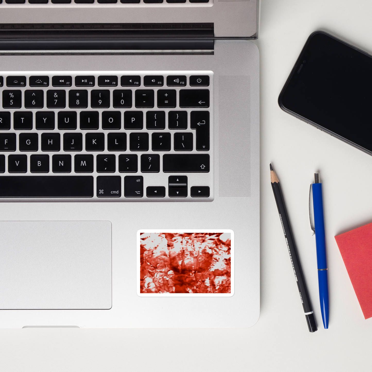 Lifestyle photo of a rectangular vinyl sticker with an image of a vivid red water reflection design, placed on a laptop to the right of the mouse pad.