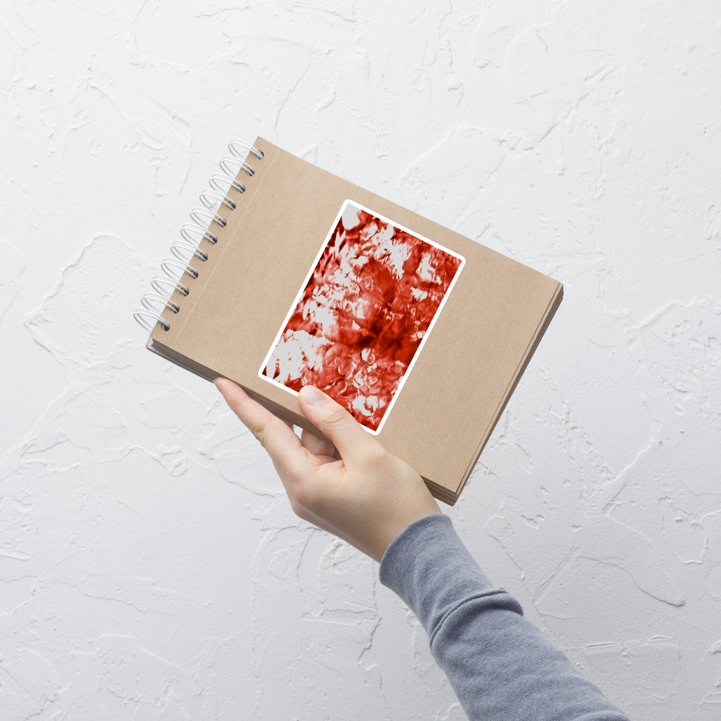 Lifestyle photo of a rectangular vinyl sticker with an image of a vivid red water reflection design, placed on a small notepad.