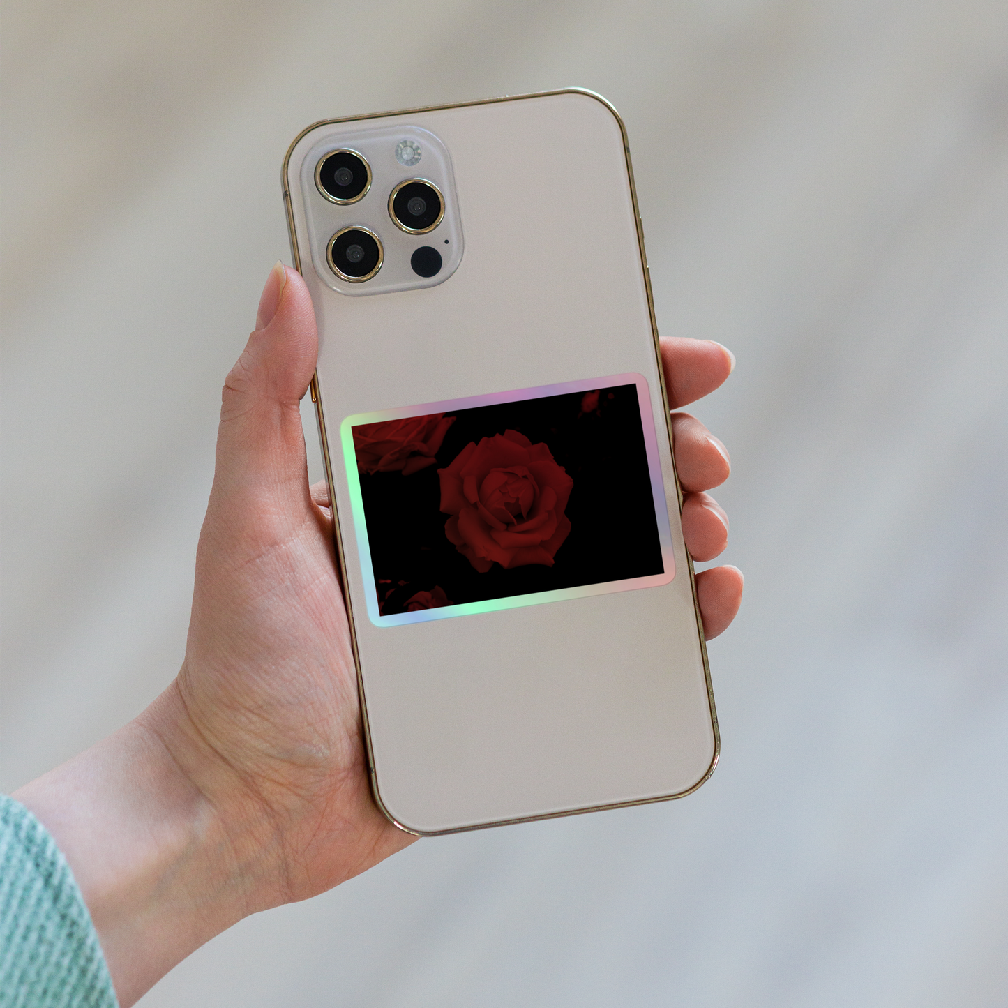 Lifestyle photo of a rectangular holographic sticker with an image of a red vivid rose design, placed on the back of a phone.