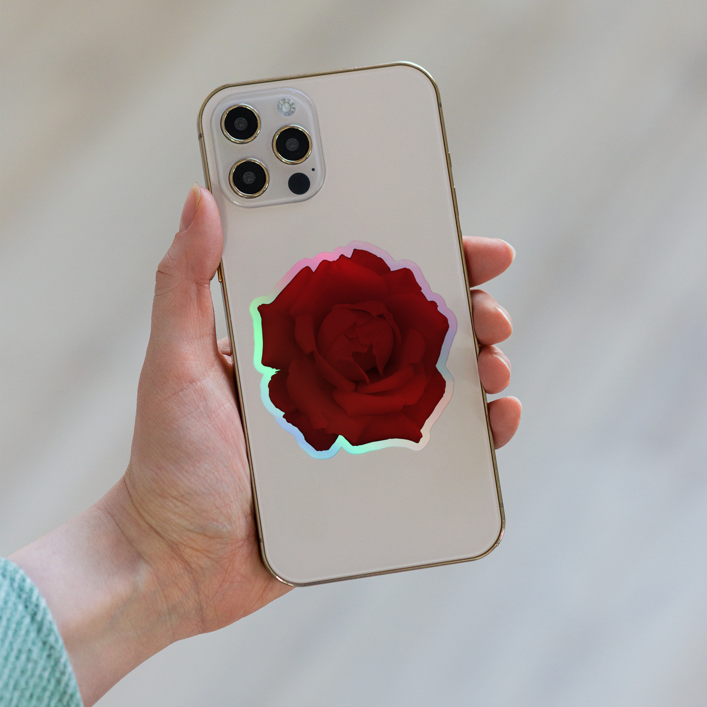 Lifestyle photo of a kiss-cut holographic sticker with an image of a vivid red rose design, placed on the back of a phone.