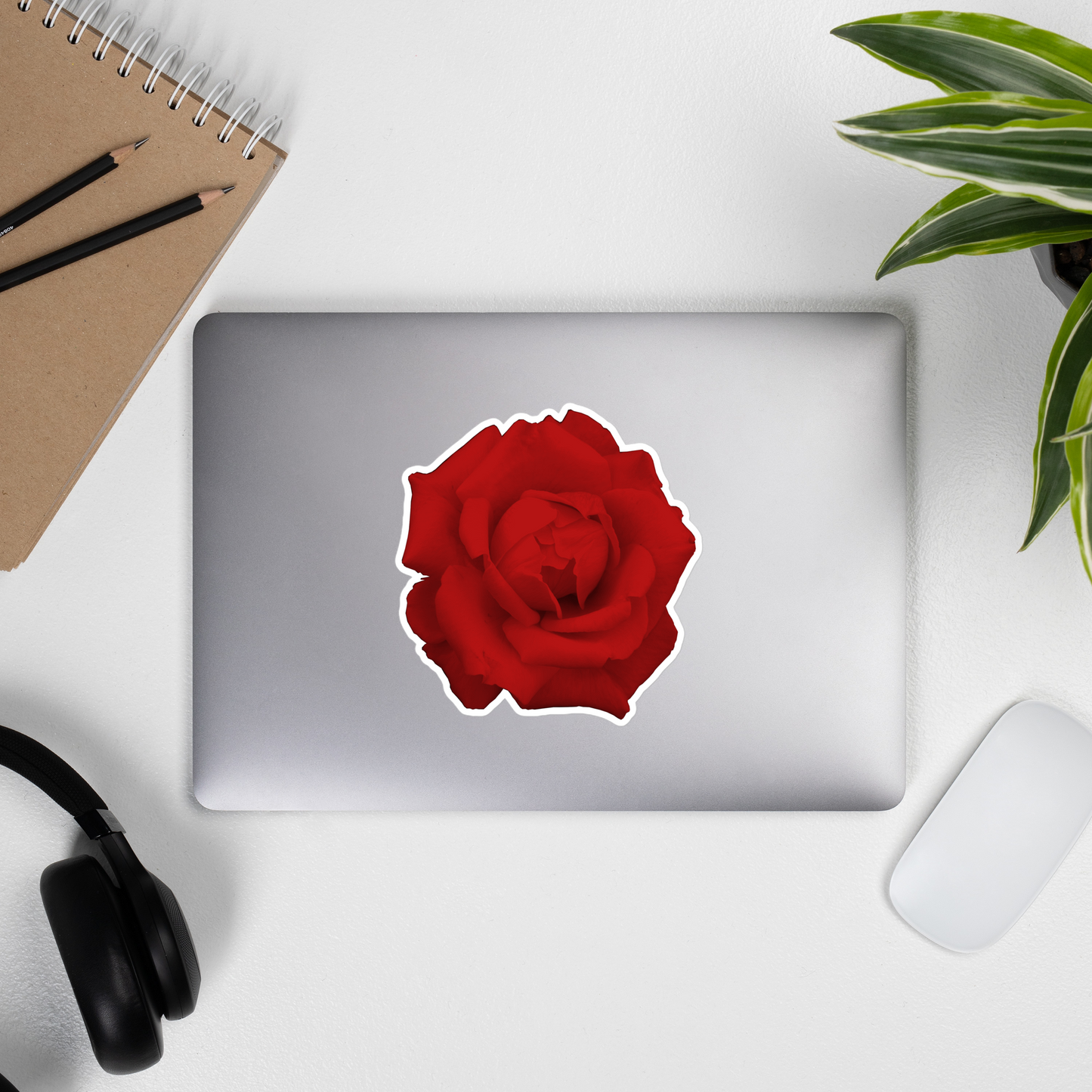 Lifestyle photo of a kiss-cut vinyl sticker with an image of a vivid red rose design, placed on the outside of a laptop.