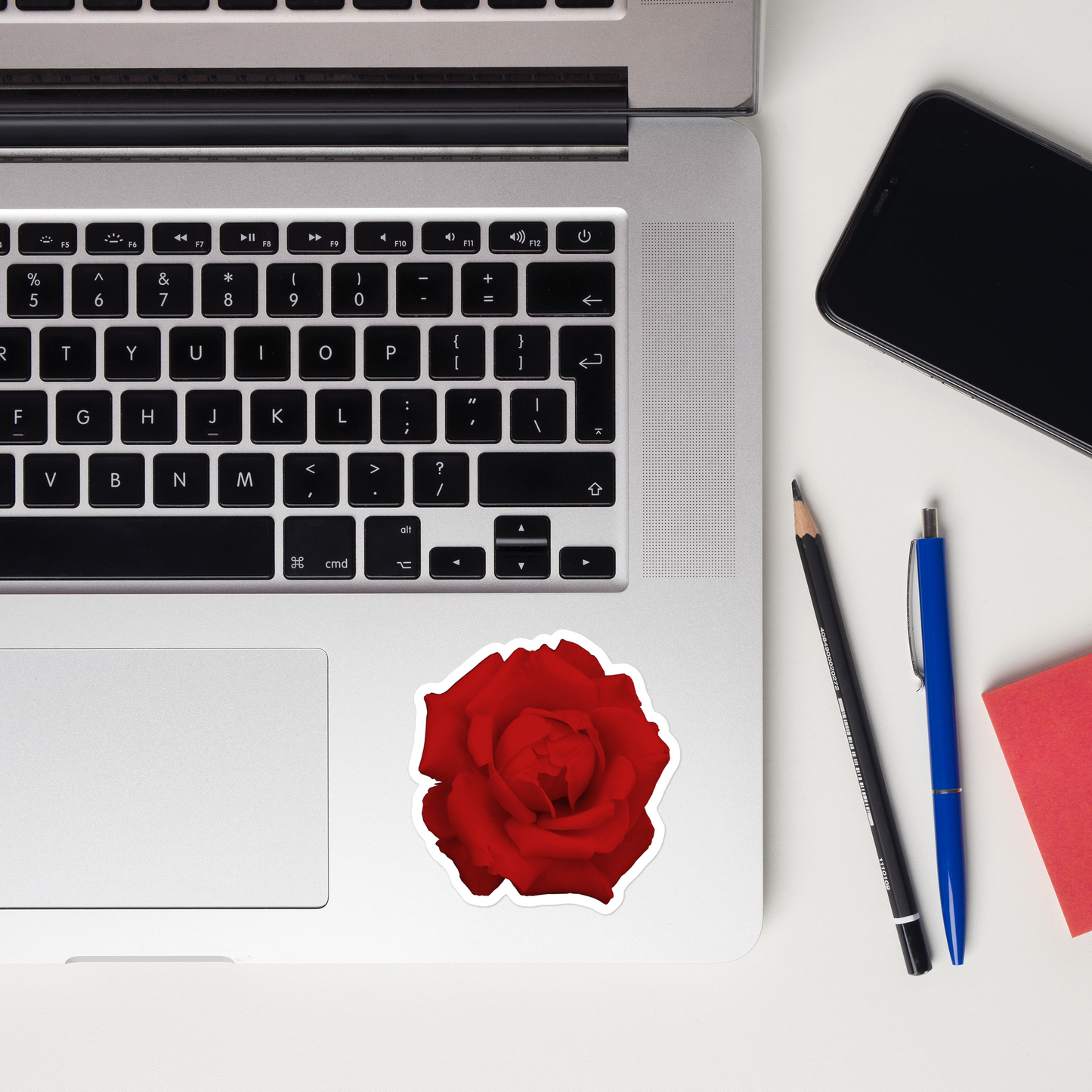 Lifestyle photo of a kiss-cut vinyl sticker with an image of a vivid red rose design, placed on a laptop to the right of the mouse pad.