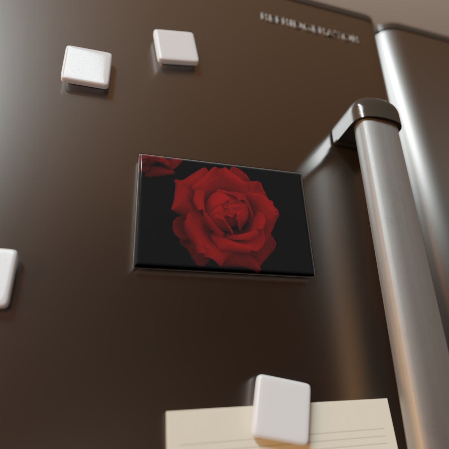 Lifestyle photo of a rectangular button magnet with an image of a vivid red rose design, placed on a fridge.