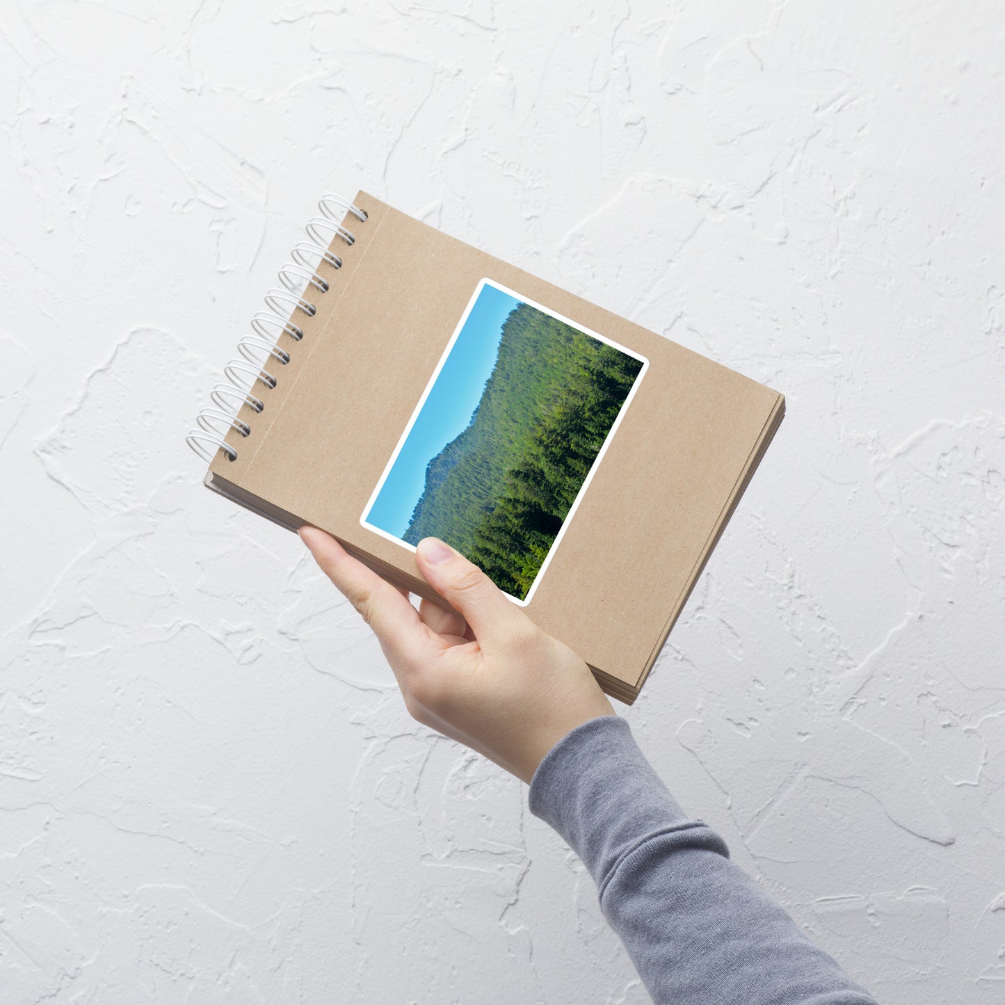 Lifestyle photo of a rectangular vinyl sticker with an image of mountain landscape with redwood trees and blue sky, placed on a small notepad.