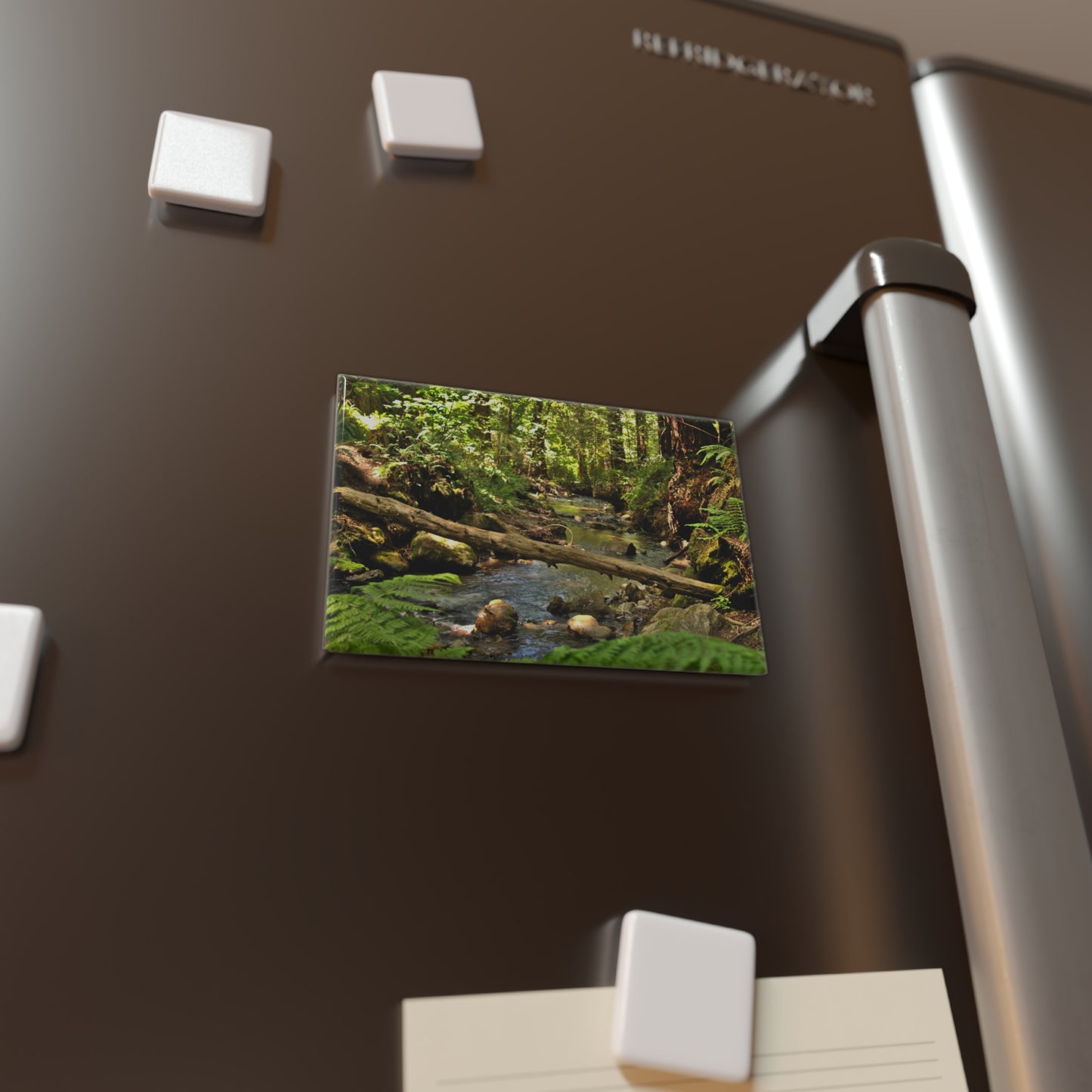 Lifestyle photo of a rectangular button magnet with an image of a serene creek in a redwood forest, placed on a fridge.