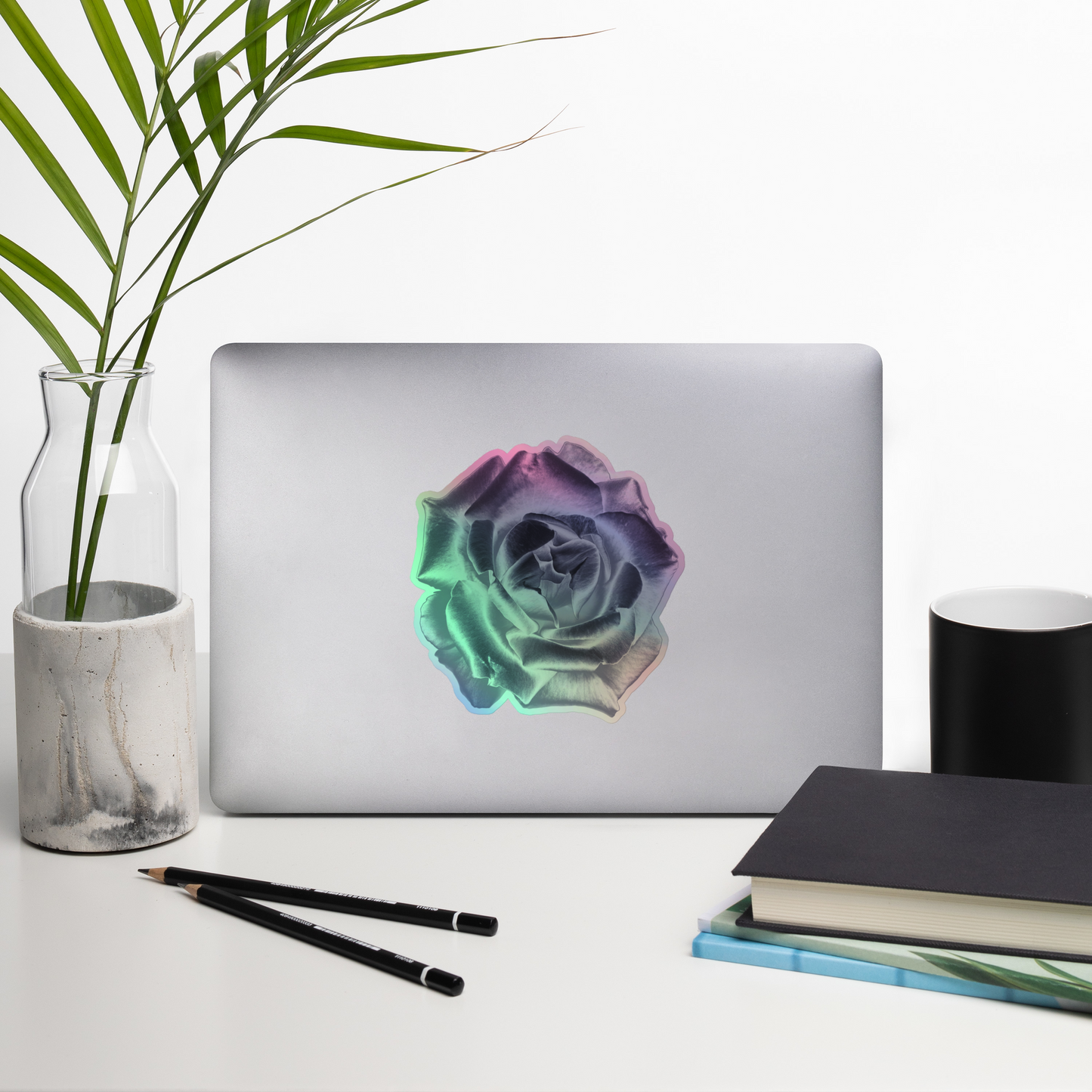 Lifestyle photo of a kiss-cut holographic sticker with an image of a reflective silver rose design, placed on a laptop with desk supplies nearby.