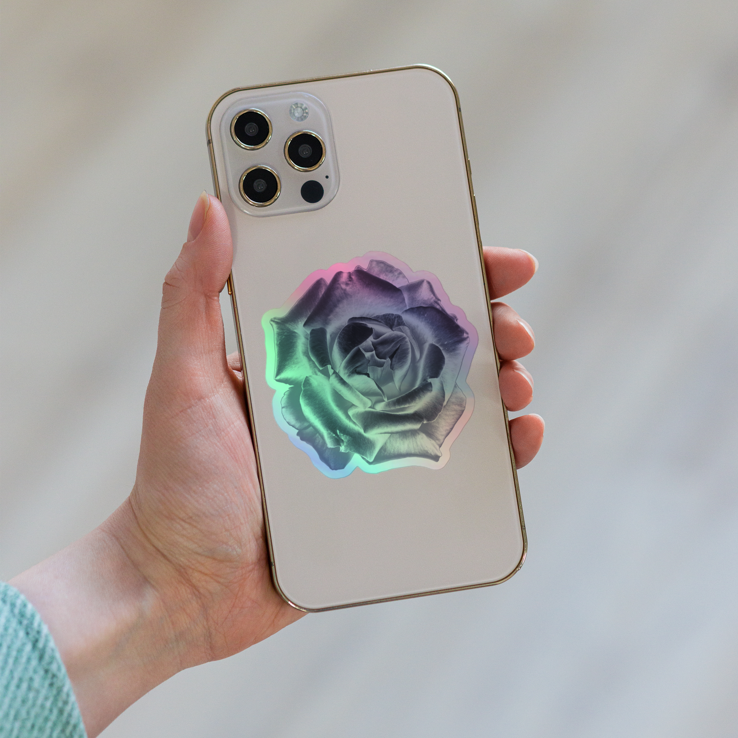 Lifestyle photo of a kiss-cut holographic sticker with an image of a reflective silver rose design, placed on the back of a phone.