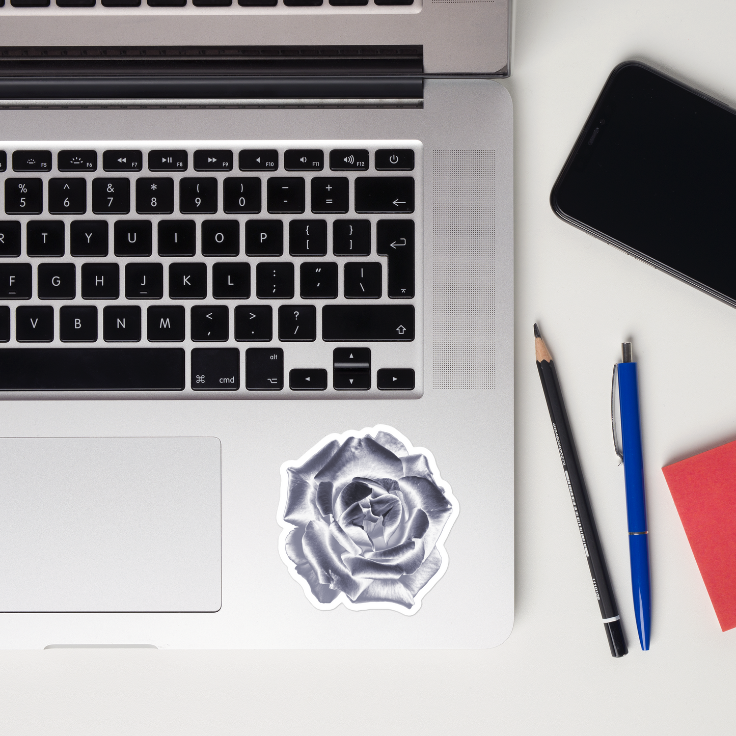 Lifestyle photo of a kiss-cut vinyl sticker with an image of a silver reflective rose, placed on a laptop to the right of the mouse pad.