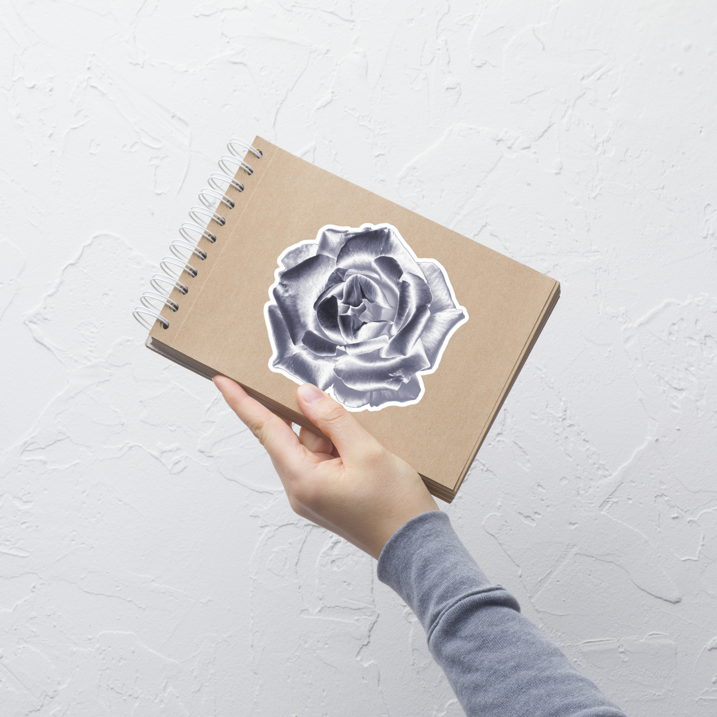 Lifestyle photo of a kiss-cut vinyl sticker with an image of a silver reflective rose, placed on a small notepad.