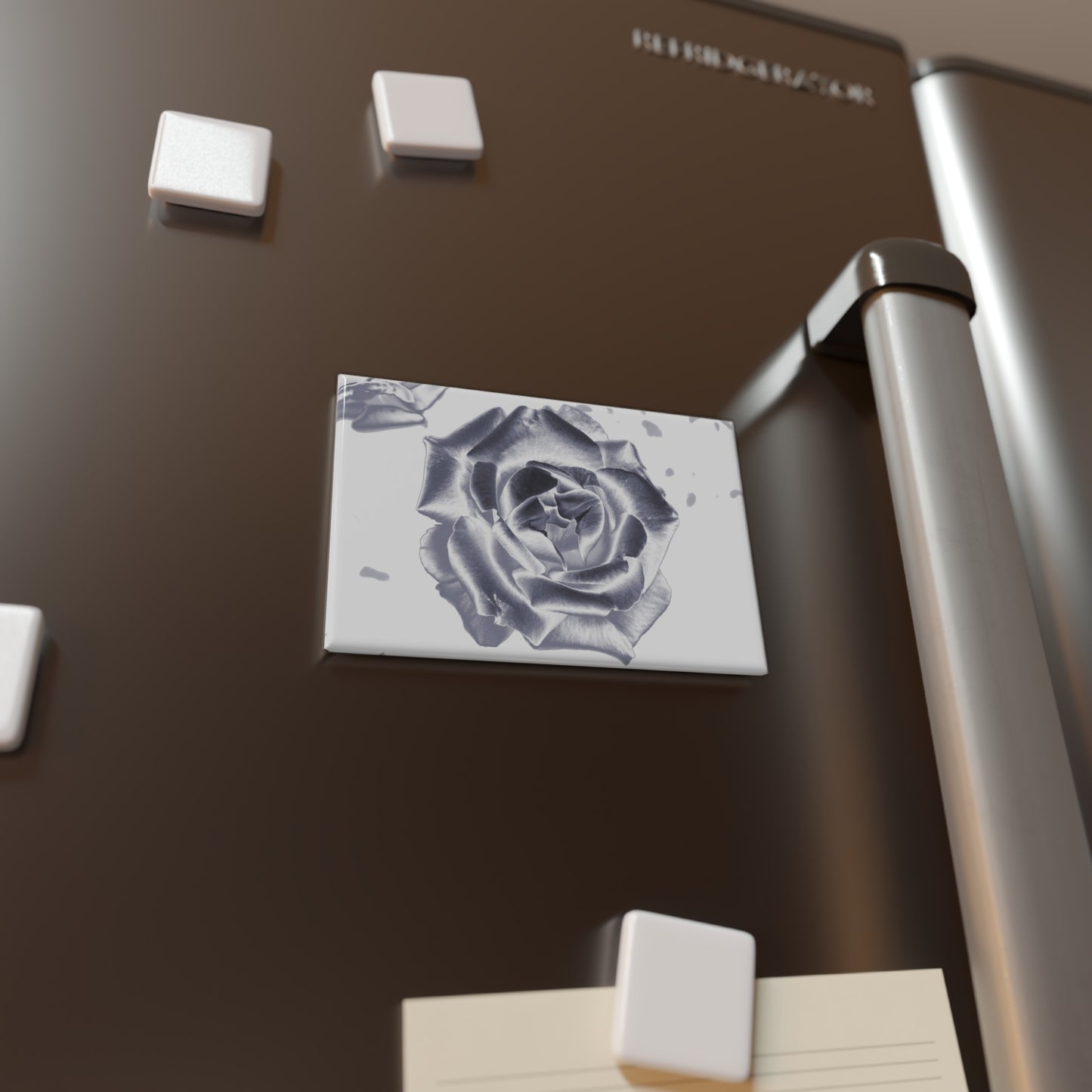 Lifestyle photo of a rectangular button magnet with an image of a silver reflective rose design, placed on a fridge.