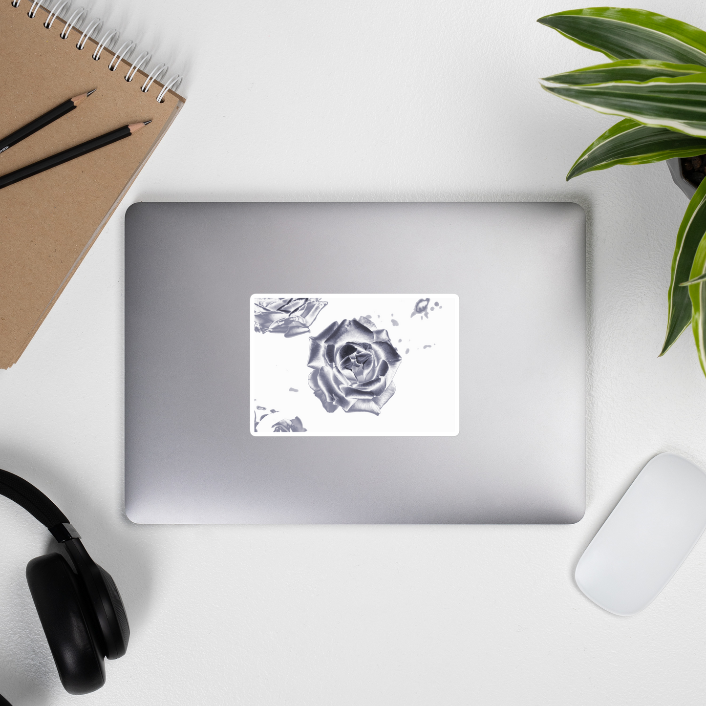 Lifestyle photo of a rectangular vinyl sticker with an image of a reflective silver rose design, placed on the outside of a laptop.