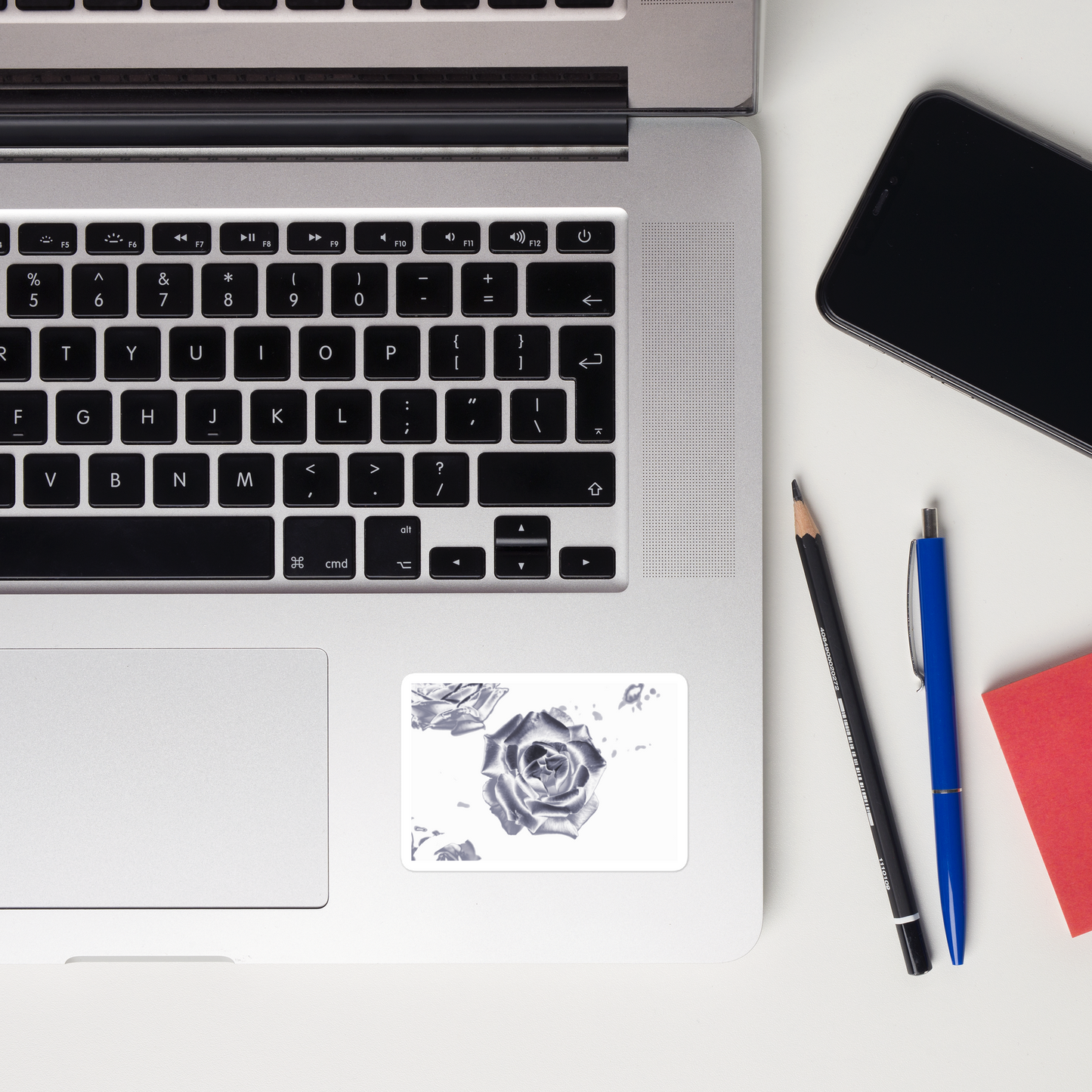 Lifestyle photo of a rectangular vinyl sticker with an image of a reflective silver rose design, placed on a laptop to the right of the mouse pad.