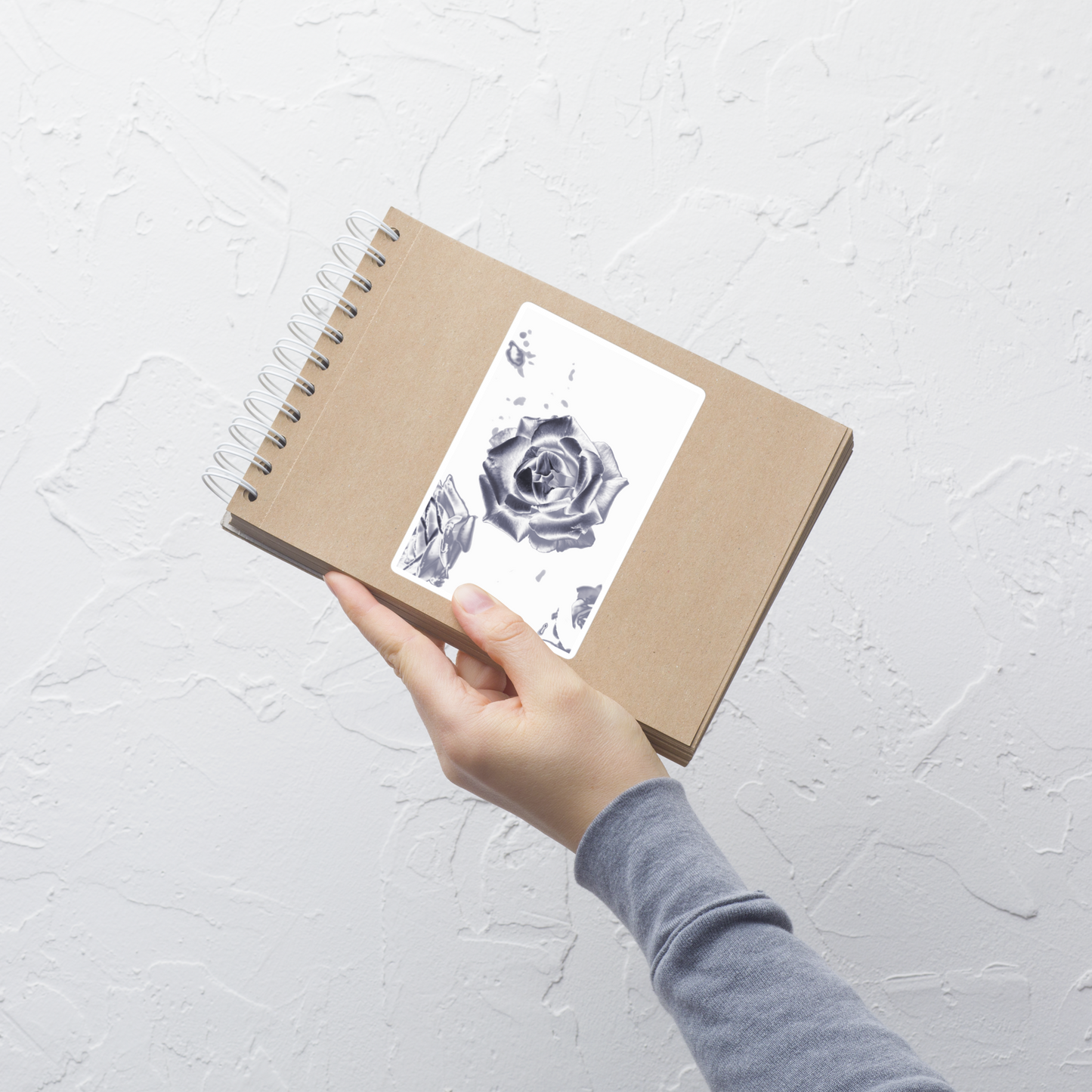 Lifestyle photo of a rectangular vinyl sticker with an image of a reflective silver rose design, placed on a small notepad.