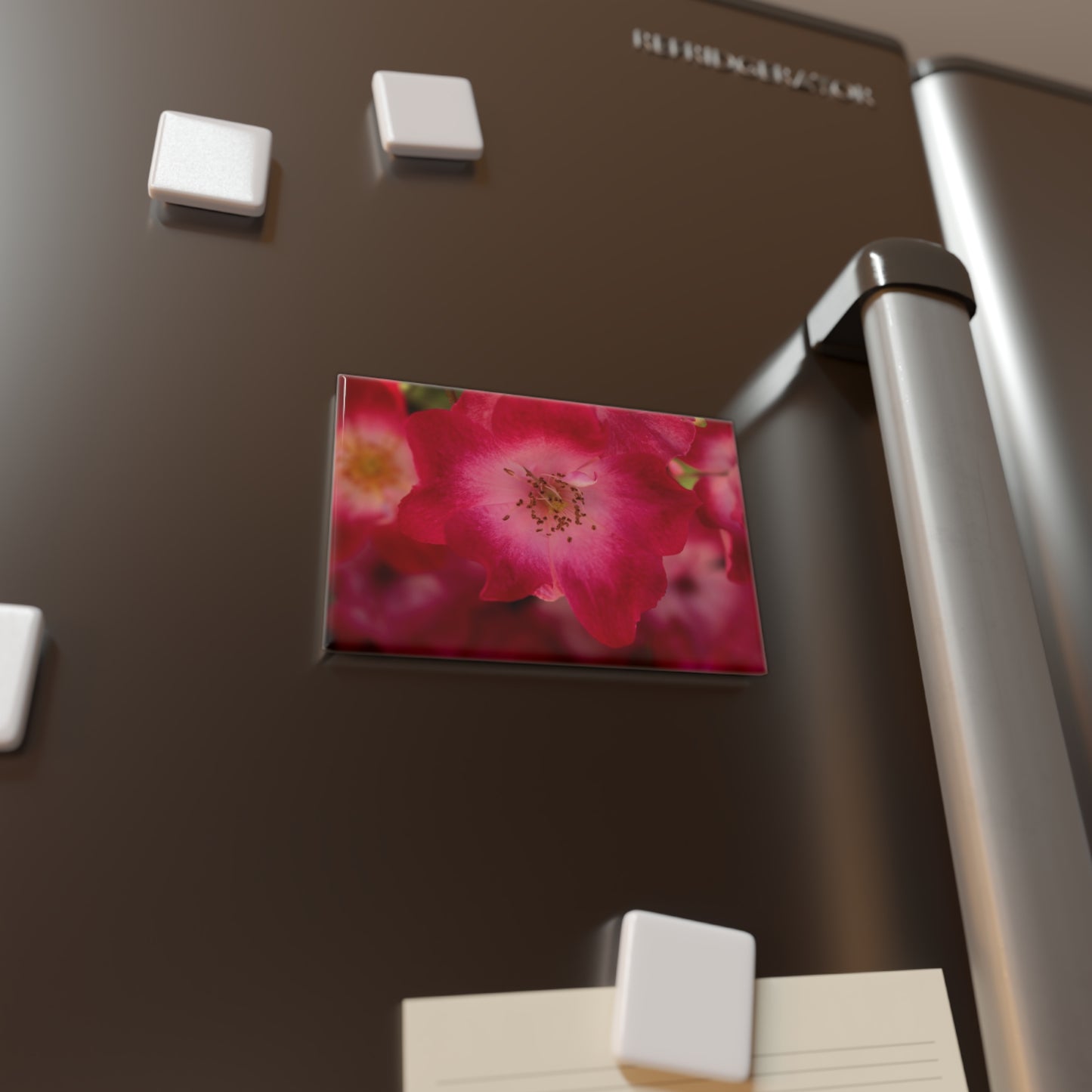 Lifestyle photo of a rectangular button magnet with an image of a pink rose with white in the center, placed on a fridge.