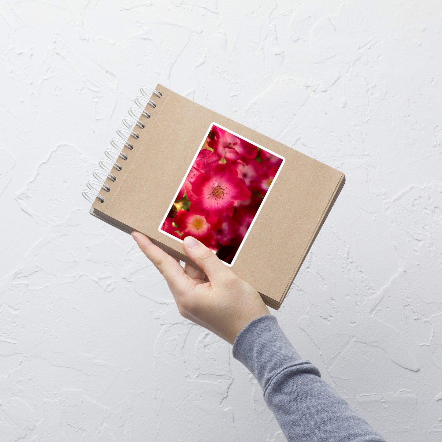 Lifestyle photo of a rectangular vinyl sticker with an image of dark pink flowers with white centers, placed on a small notepad.