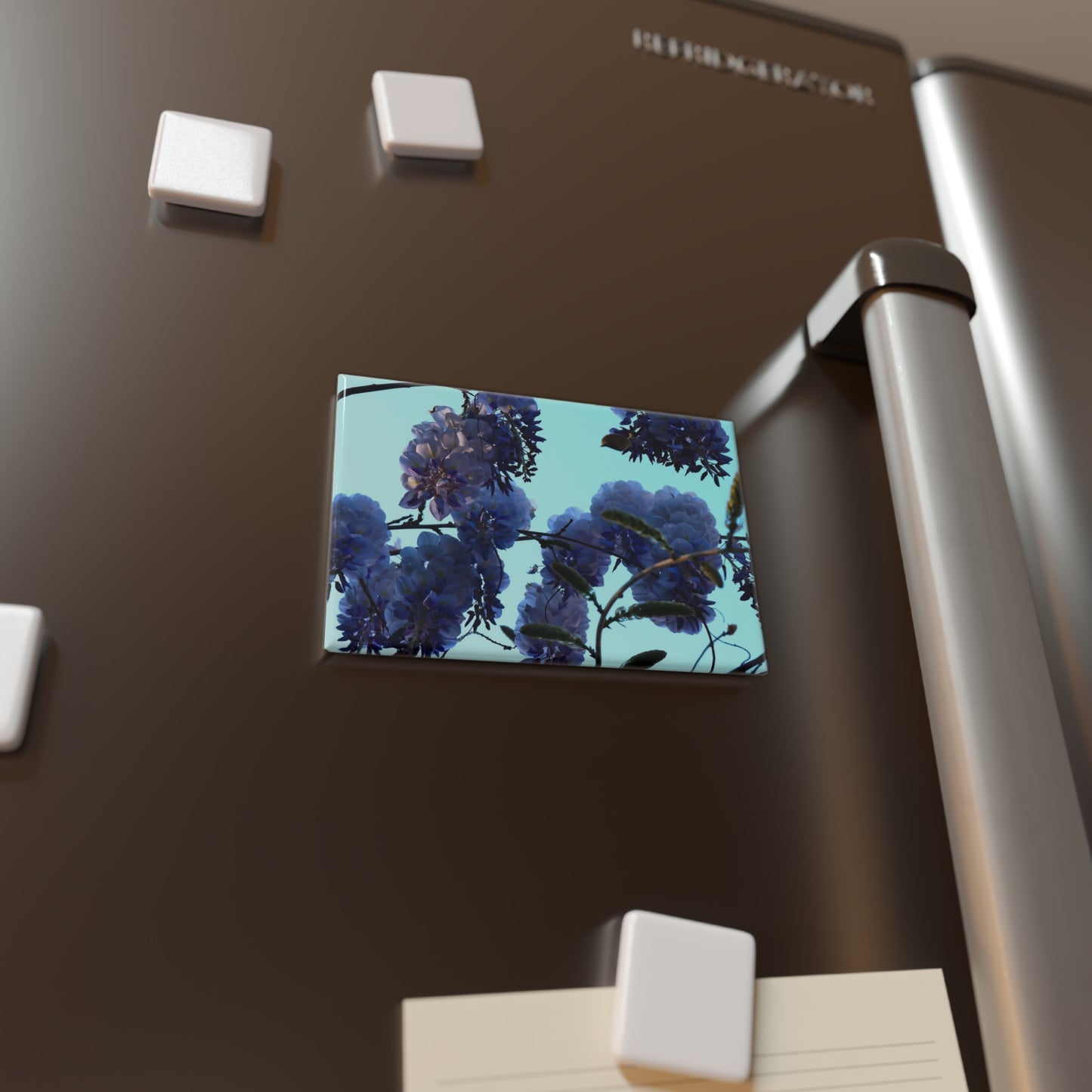 Lifestyle photo of a rectangular button magnet featuring an image of purple wisteria blossoms against a clear blue sky, placed on a fridge.