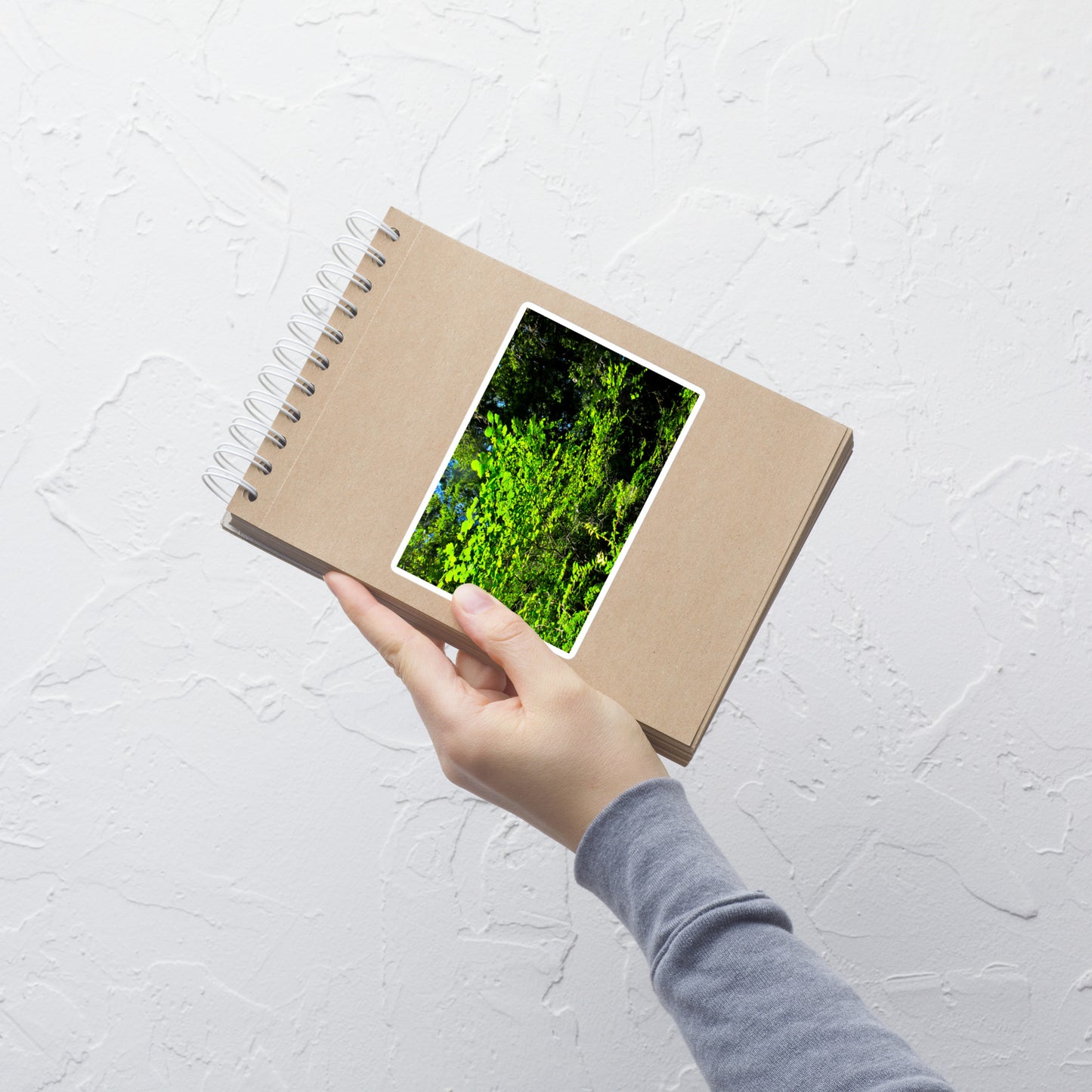 Lifestyle photo of a rectangular vinyl sticker with an image of backlit bright green tree leaves, placed on a small notepad.