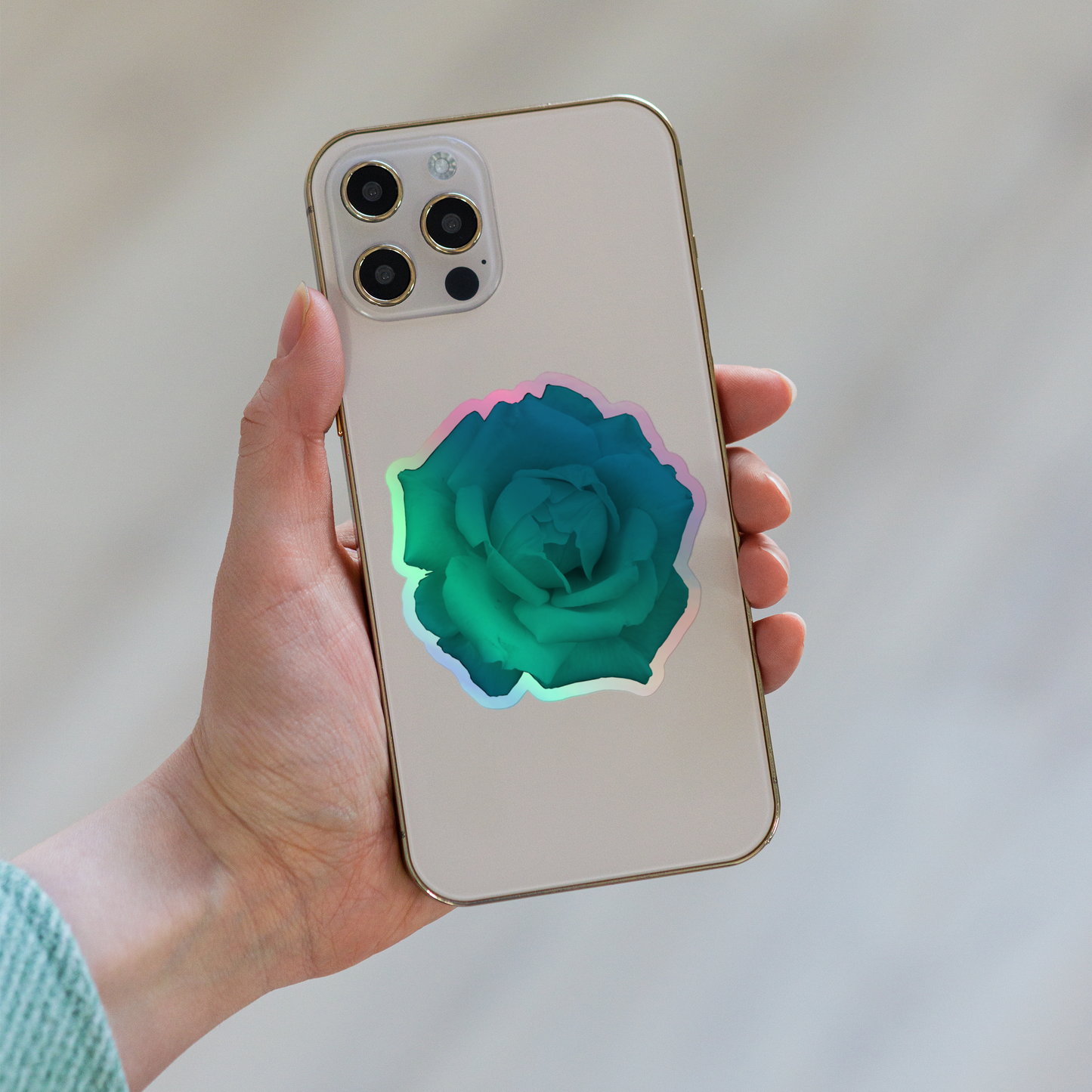 Lifestyle photo of a kiss-cut holographic sticker with an image of a vivid turquoise rose design, placed on the back of a phone.