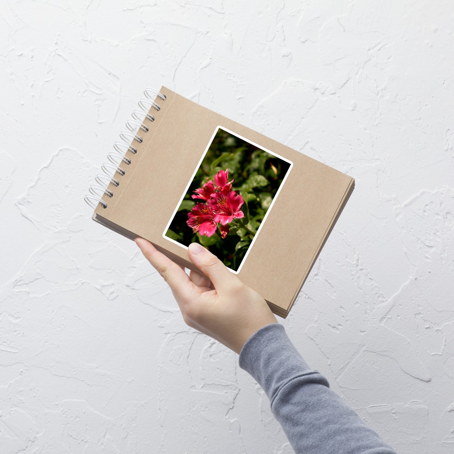 Lifestyle photo of a rectangular vinyl sticker with an image of a pink lily blooms with yellow accents, placed on a small notepad.