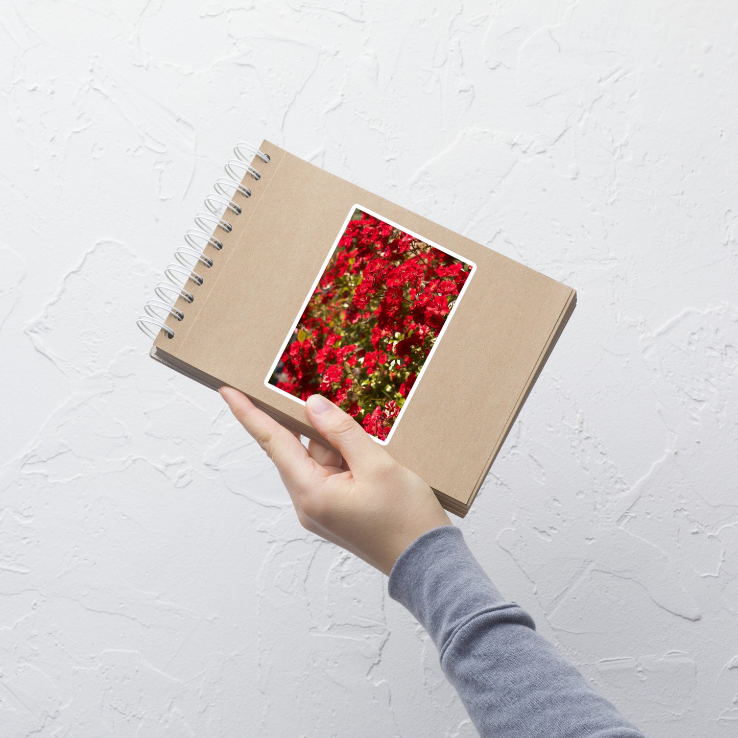 Lifestyle photo of a rectangular vinyl sticker with an image of a bush of bright red flowers, placed on a small notepad.