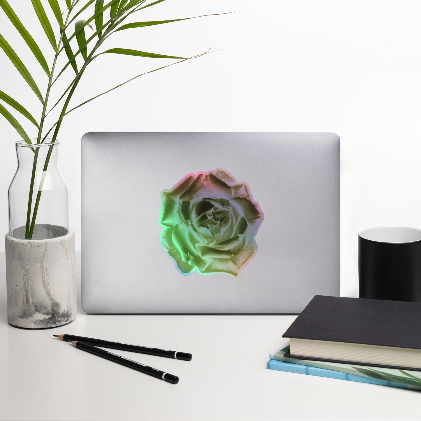 Lifestyle photo of a kiss-cut holographic sticker with an image of a reflective yellow rose design, placed on a laptop with desk supplies nearby.