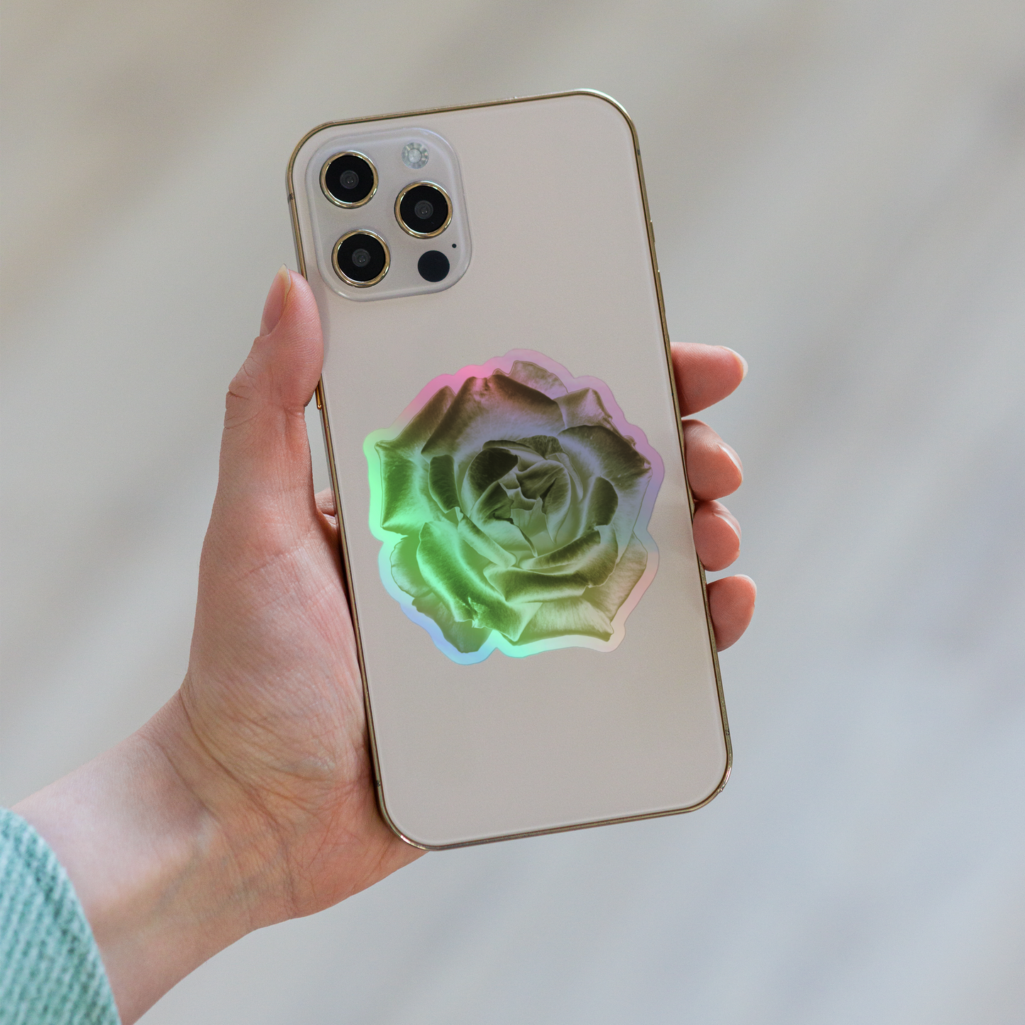 Lifestyle photo of a kiss-cut holographic sticker with an image of a reflective yellow rose design, placed on the back of a phone.