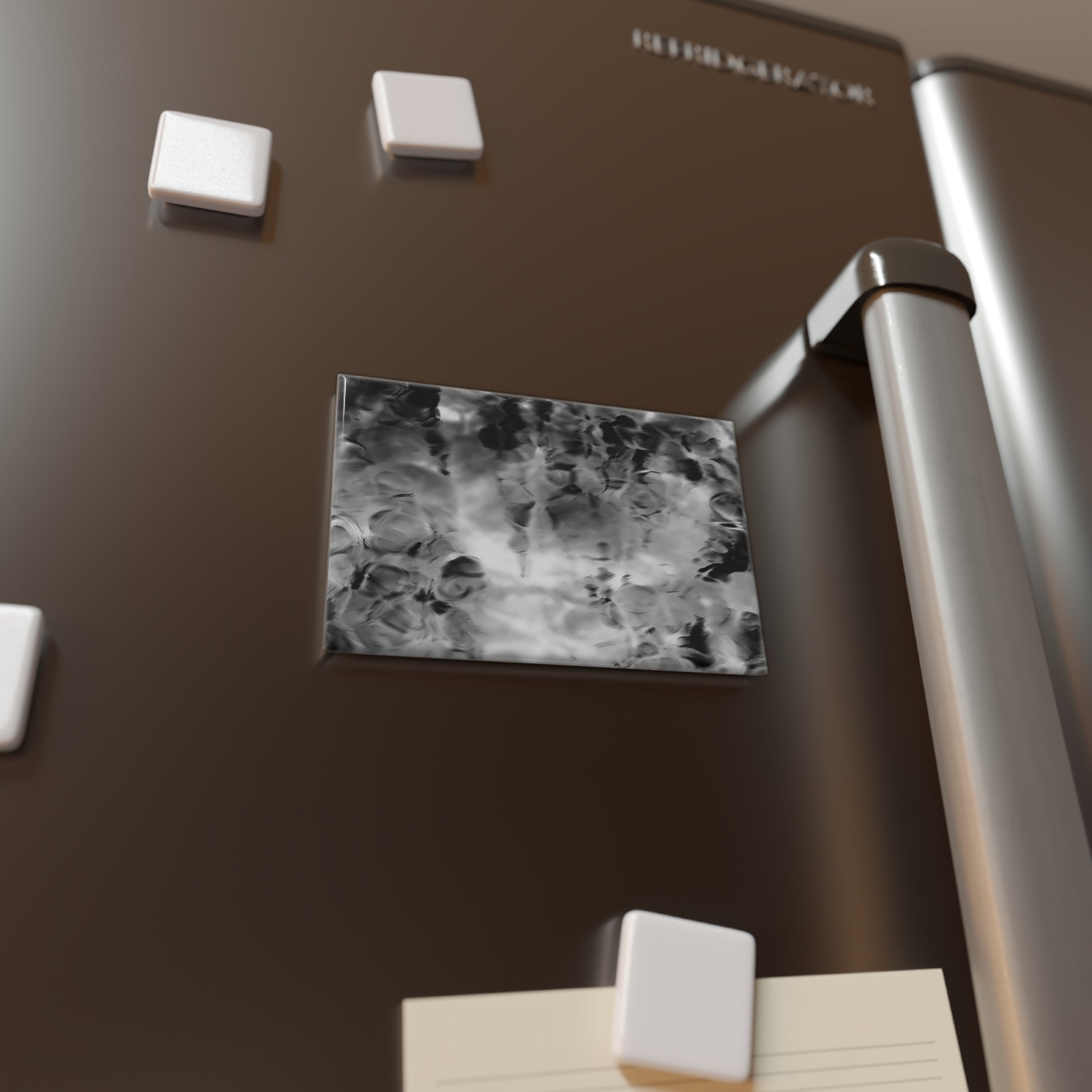 Lifestyle photo of a rectangular button magnet with an image of a vivid black and white water reflection design, placed on a fridge.