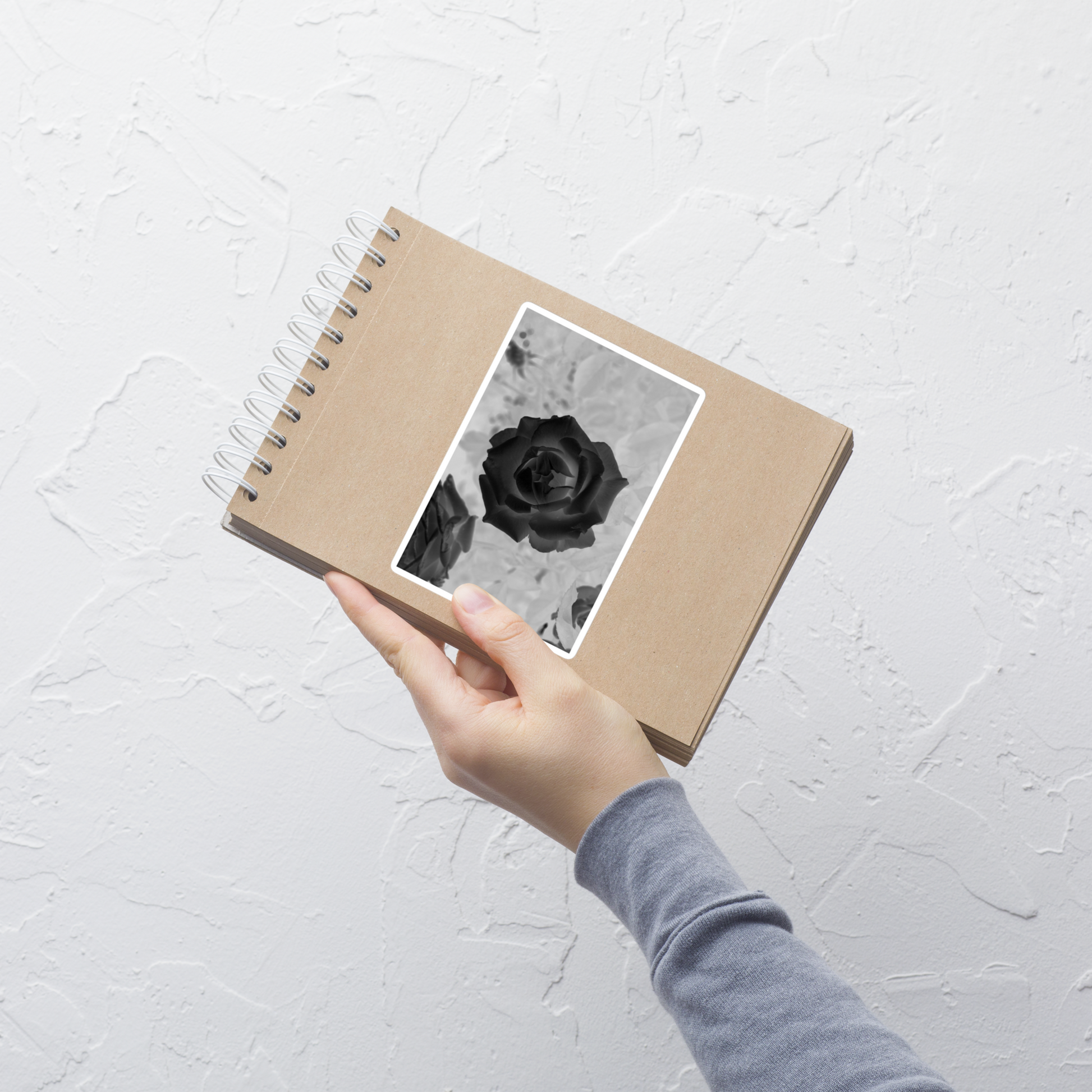 Lifestyle photo of a rectangular vinyl sticker with an image of a black x-ray rose design, placed on a small notepad.