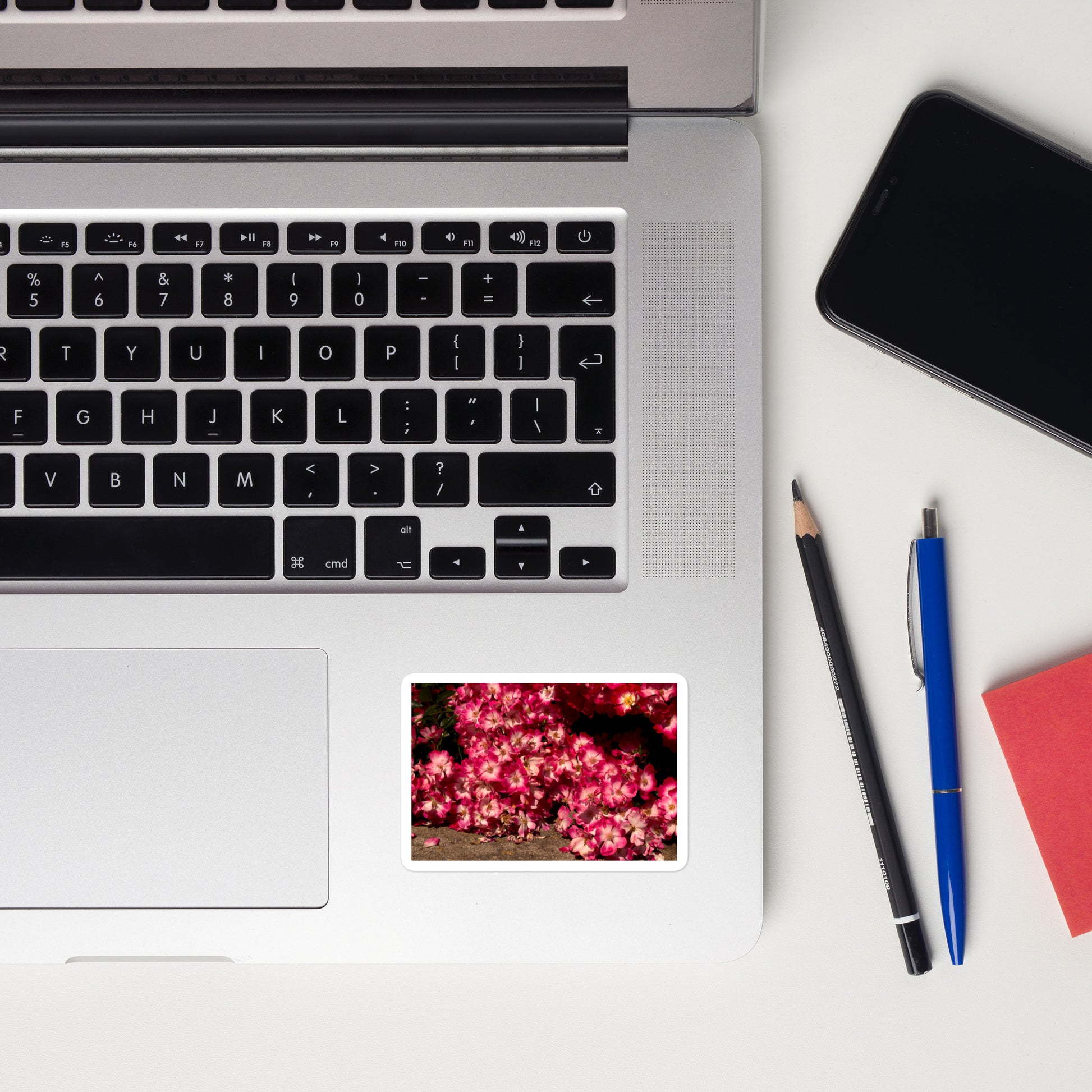 Lifestyle photo of a rectangular vinyl sticker with an image of many small pink flowers with white centers, placed on a laptop to the right of the mouse pad.