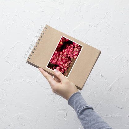 Lifestyle photo of a rectangular vinyl sticker with an image of many small pink flowers with white centers, placed on a small notepad.