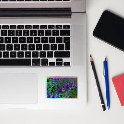 Lifestyle photo of a rectangular holographic sticker with a close-up image of bright green purple sage with green leaves, placed on a laptop to the right of the mouse pad.