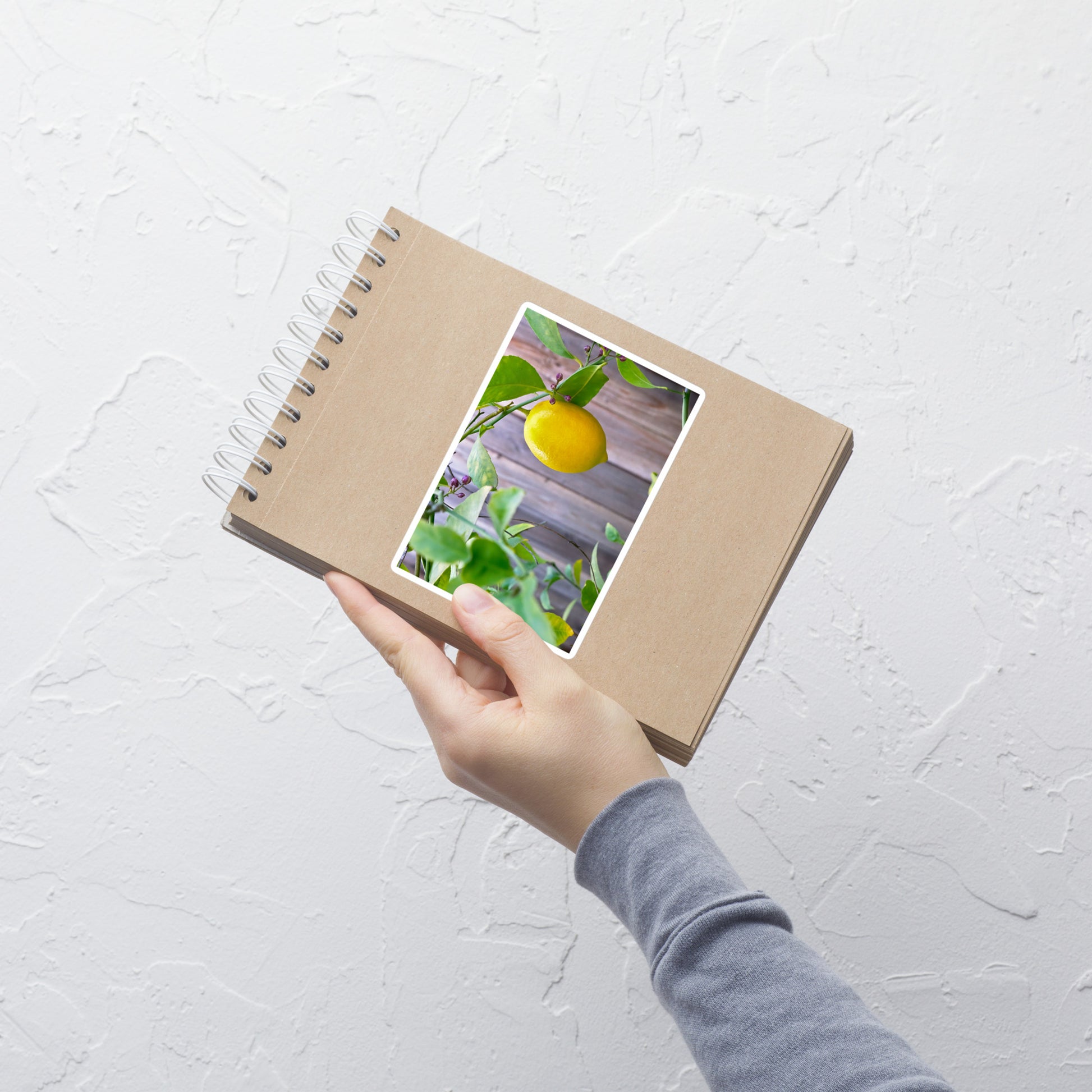 Lifestyle photo of a rectangular vinyl sticker with an image of a bright yellow lemon budding branches, placed on a small notepad.